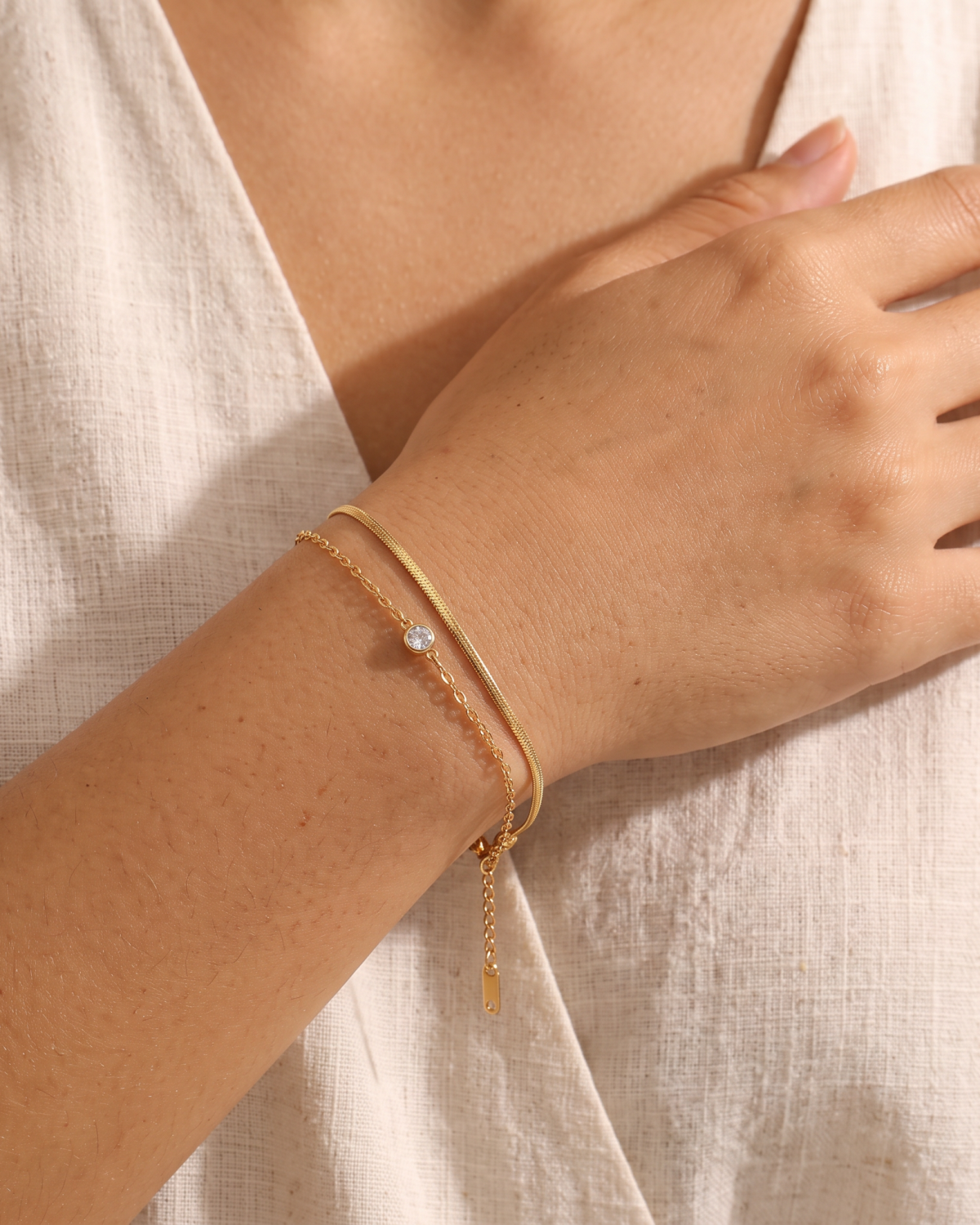 Gold-tone double-chain bracelet with a central stone accent, worn beside a white cuff.