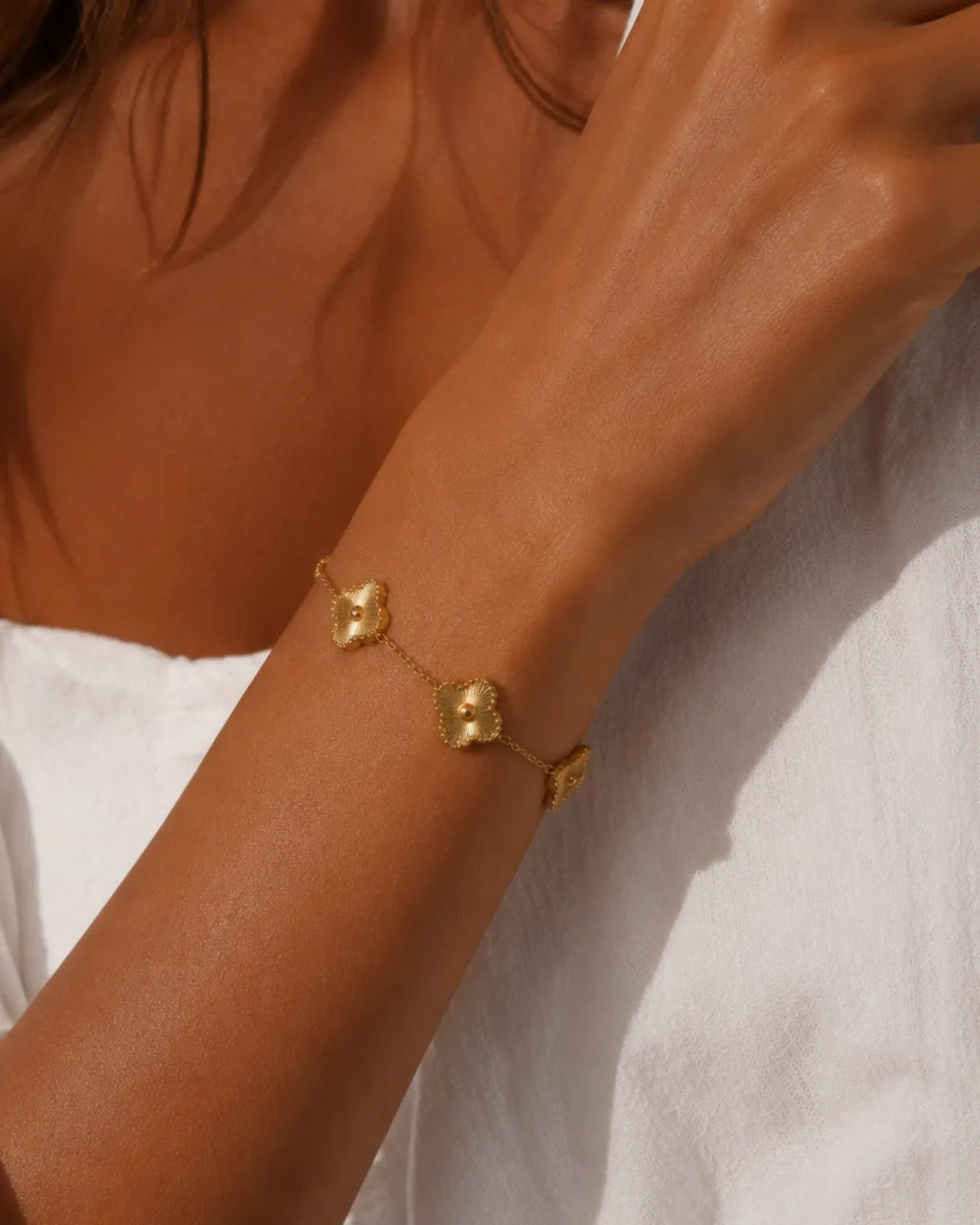 Close view of sunburst-textured clover stations on a gold-tone chain bracelet