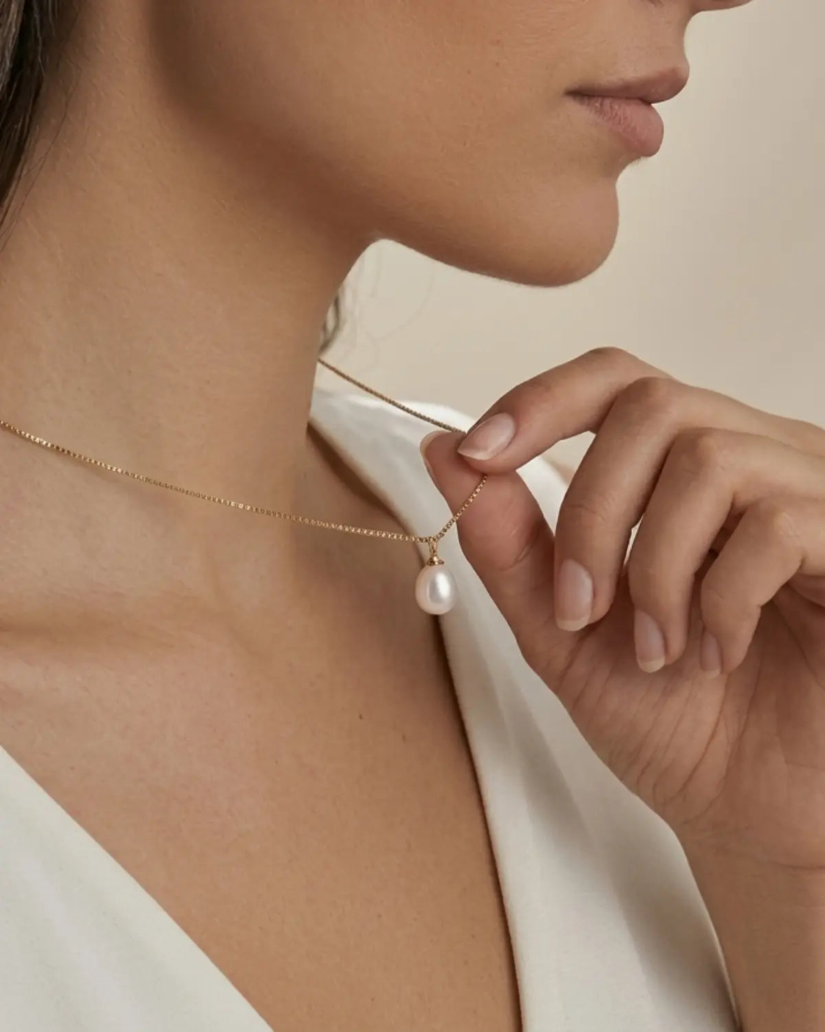 Gold-tone necklace with a white drop pendant, pendant held between fingers while worn.
