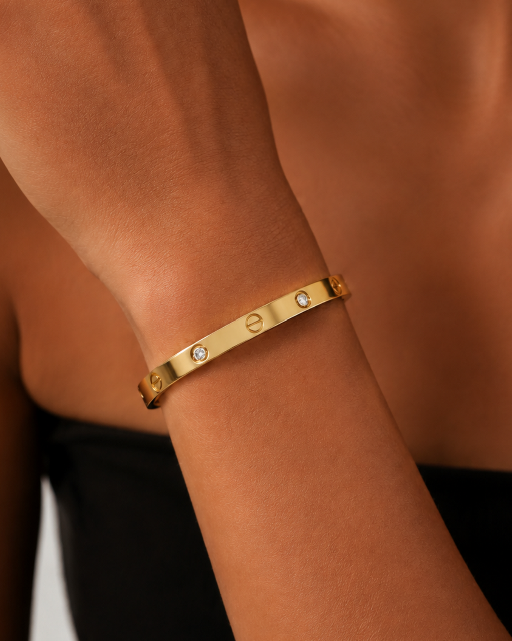 Gold-tone bangle with screw motifs and alternating stone accents, worn on a raised forearm against black clothing.