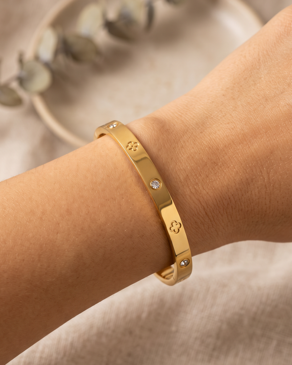 Gold-tone bangle with clover outlines and stone accents, angled close-up on the wrist.