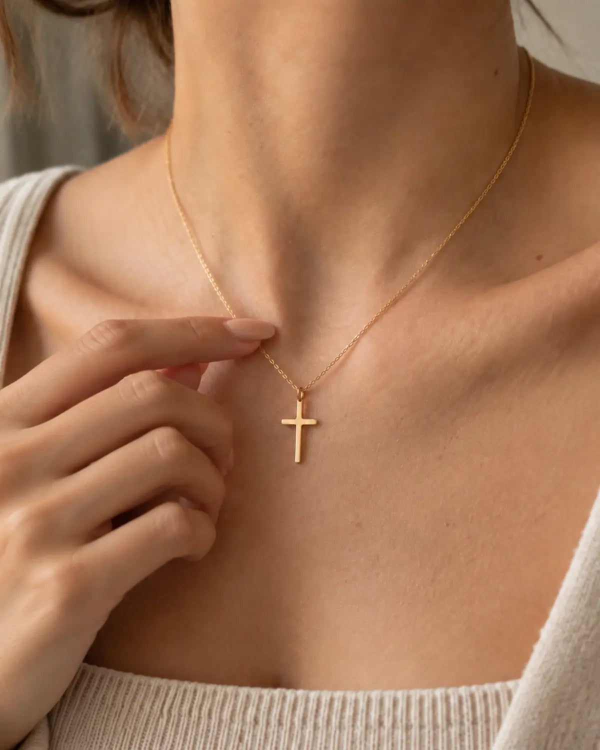 Gold-tone cross necklace worn while a hand lightly holds the chain.