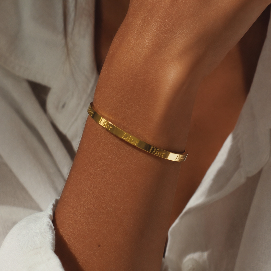 Gold-tone engraved lettering bangle worn on a wrist.