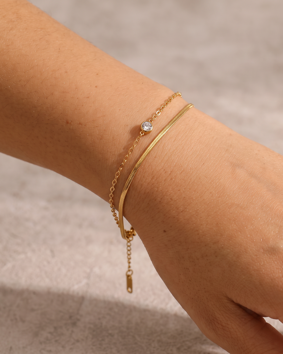 Gold-tone double-chain bracelet with a central stone accent, close-up on the wrist with the extension chain hanging below.