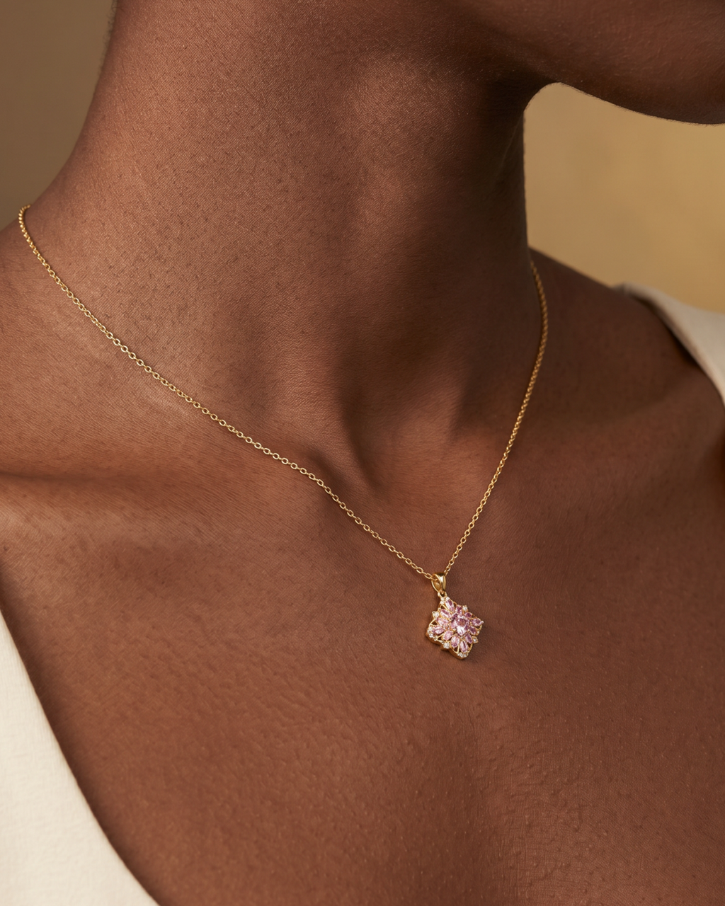 Gold-tone necklace with a pink flower pendant, worn at the neckline.
