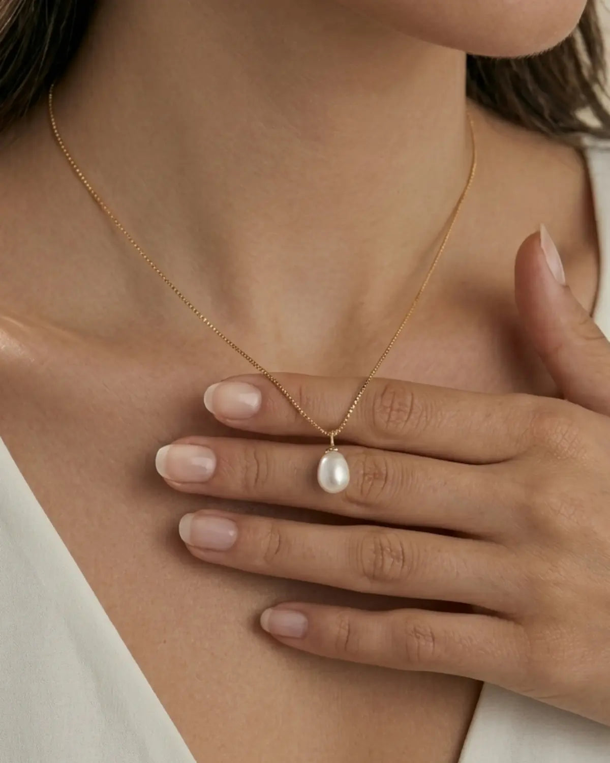 Gold-tone necklace with a white drop pendant, worn with a hand resting below the pendant.