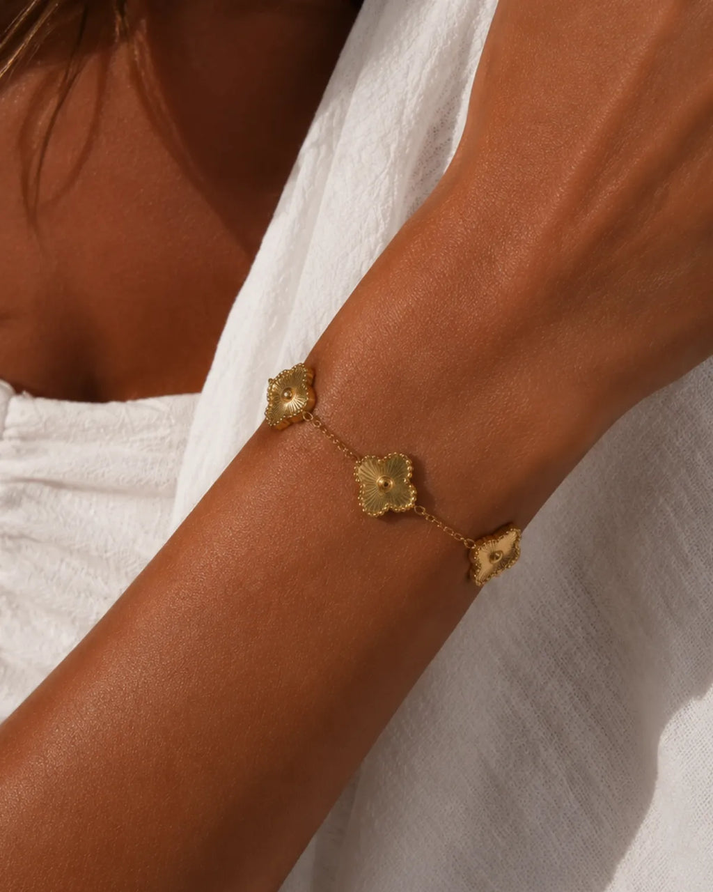 Gold-tone clover chain bracelet with sunburst-textured stations worn on a wrist