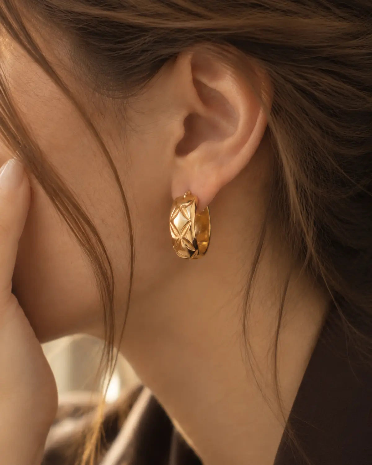 Close-up of a quilted gold-tone huggie earring on the ear.
