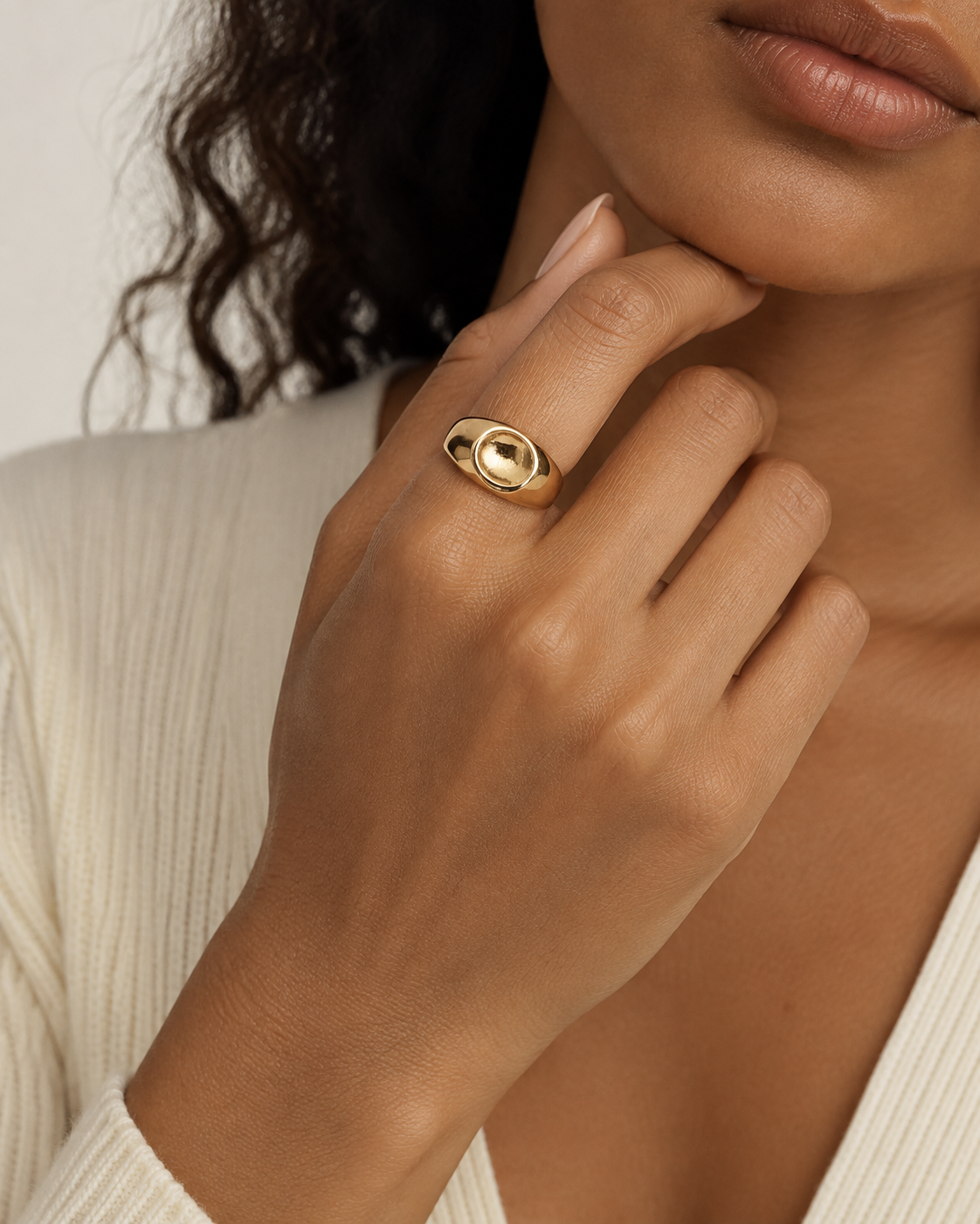 Gold-tone dome ring with a concave circular centre, close-up on a hand near the chin.