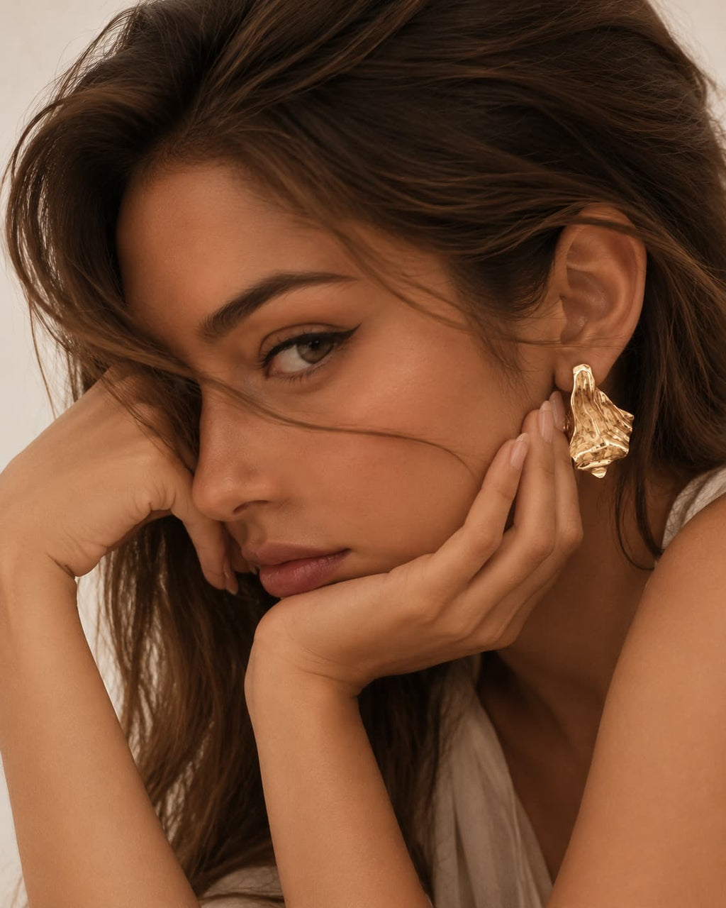 Flared gold-tone earring worn with the head supported by a hand.