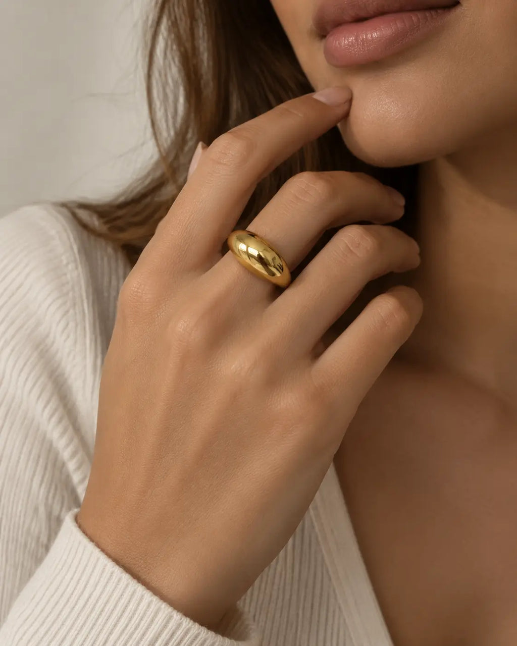 Gold-tone wide dome band ring, worn on a hand near the chin.