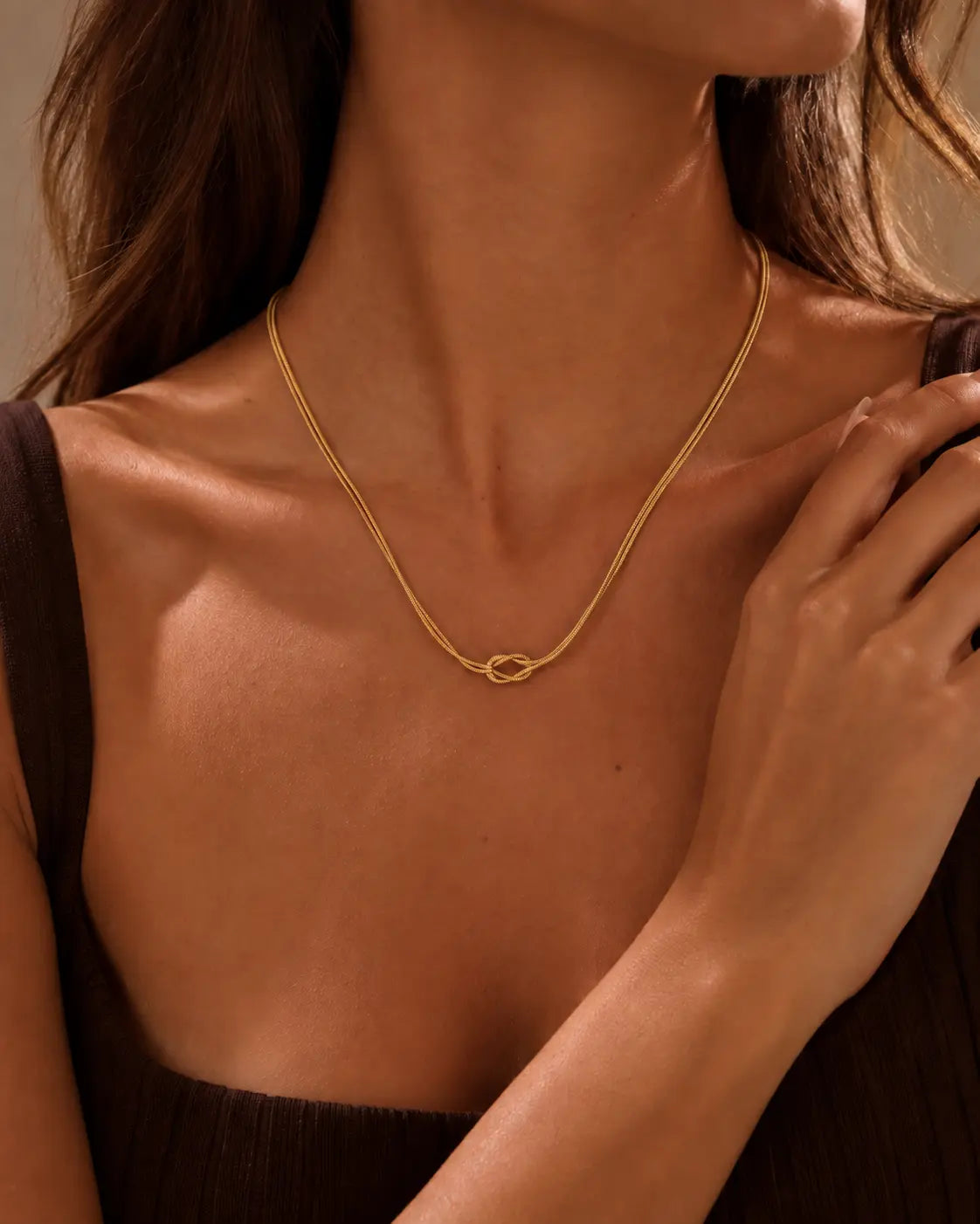 Gold-tone double-chain necklace with a central knot, worn at a black neckline with a hand near the shoulder.