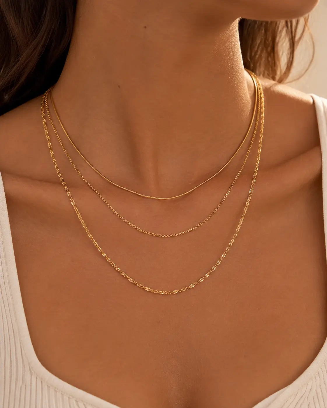 Set of three gold-tone chain necklaces in graduated lengths, worn in layers with a white top.