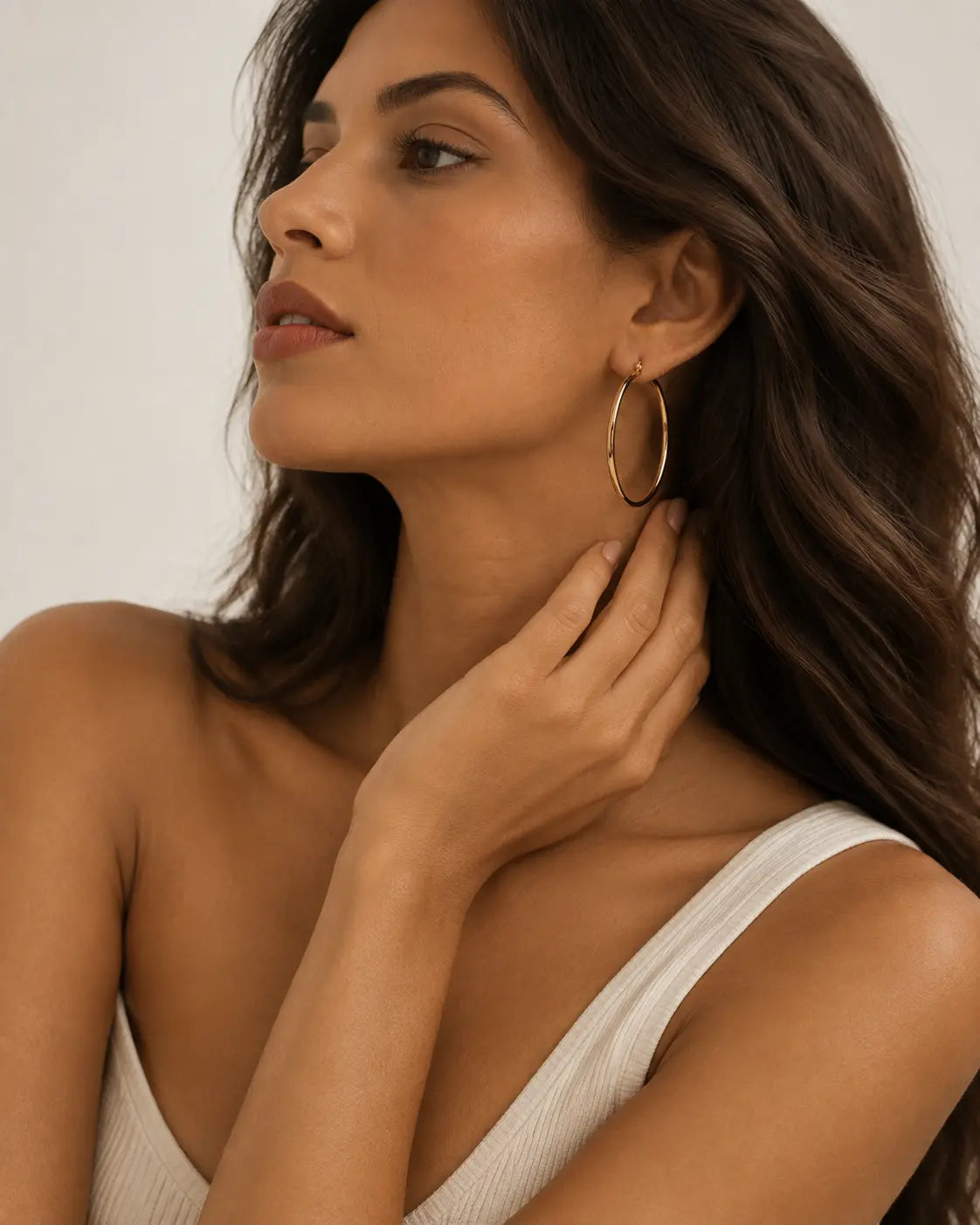 Slim gold-tone hoop earrings worn with a hand near the neck.