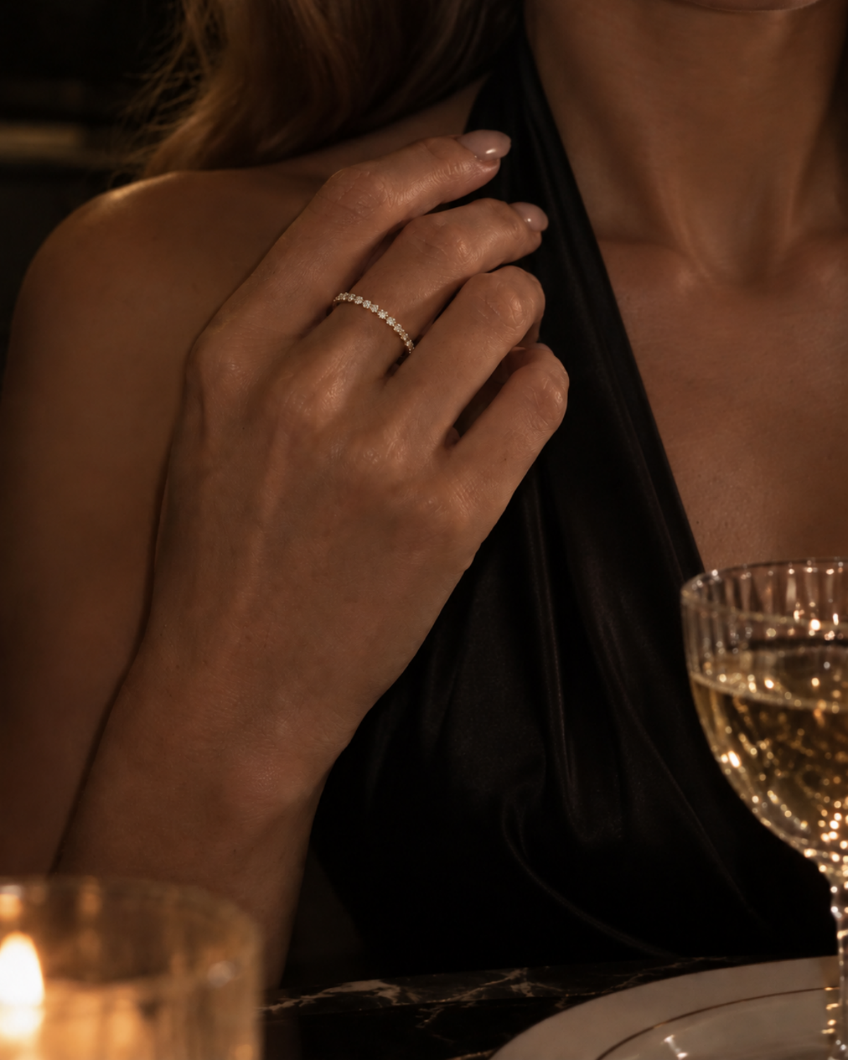 Gold-tone straight band ring with a row of pavé-style stone accents, worn on a hand beside a glass.