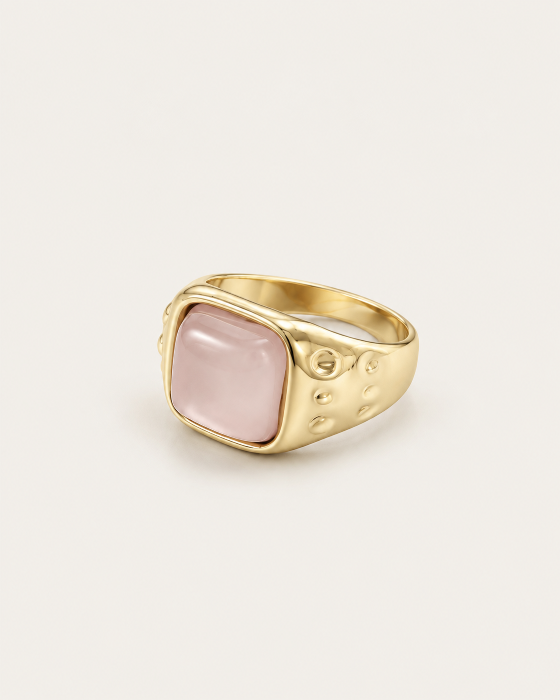 Gold-tone ring with a pale pink cushion-shaped accent, angled view showing the textured shoulders.
