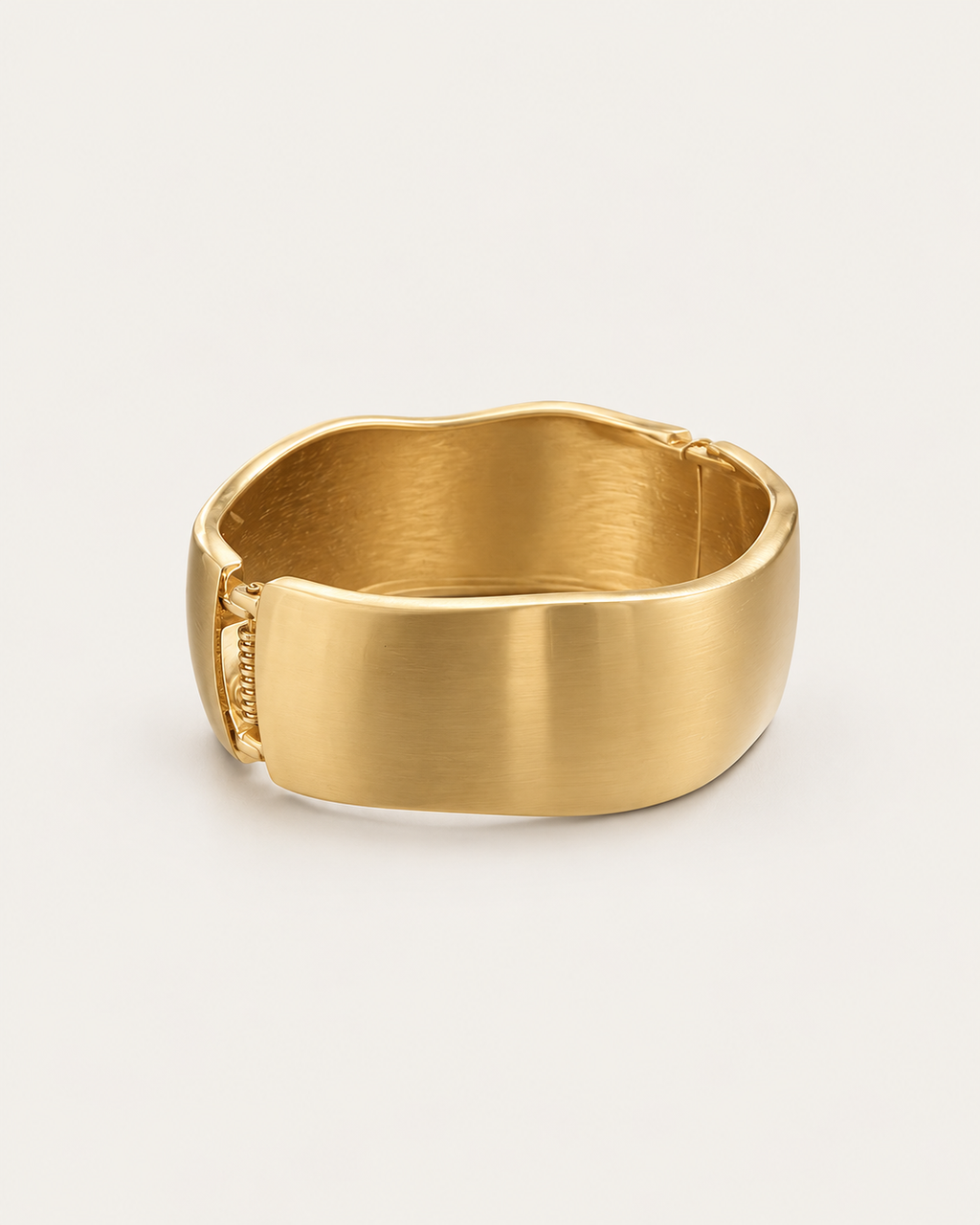 Gold-tone wide bangle with a satin-looking surface and wavy edges, angled view showing the clasp area.