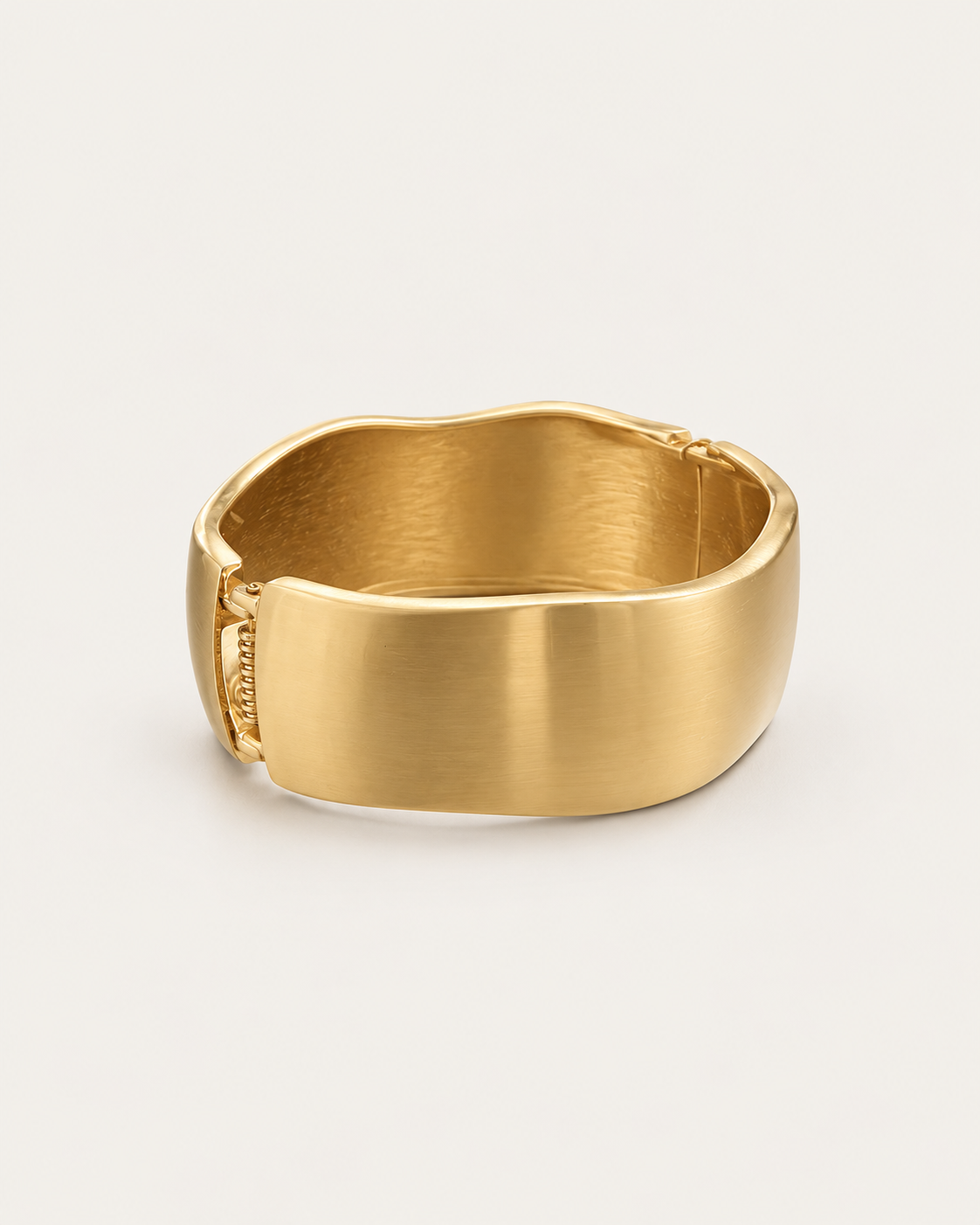 Gold-tone wide bangle with a satin-looking surface and wavy edges, angled view showing the clasp area.