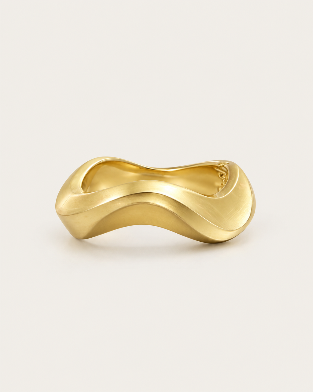 Gold-tone sculptural bangle with an undulating outline, angled view showing the inner curve.