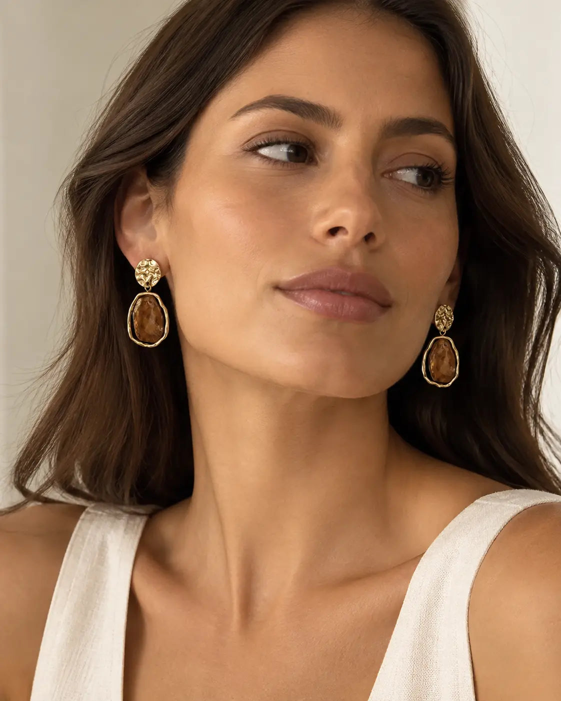 Faceted brown drop earrings worn in a three-quarter portrait.
