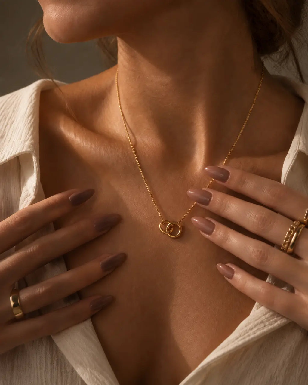 Gold-tone necklace with two interlocking circle pendants, worn with hands framing the linked circles.