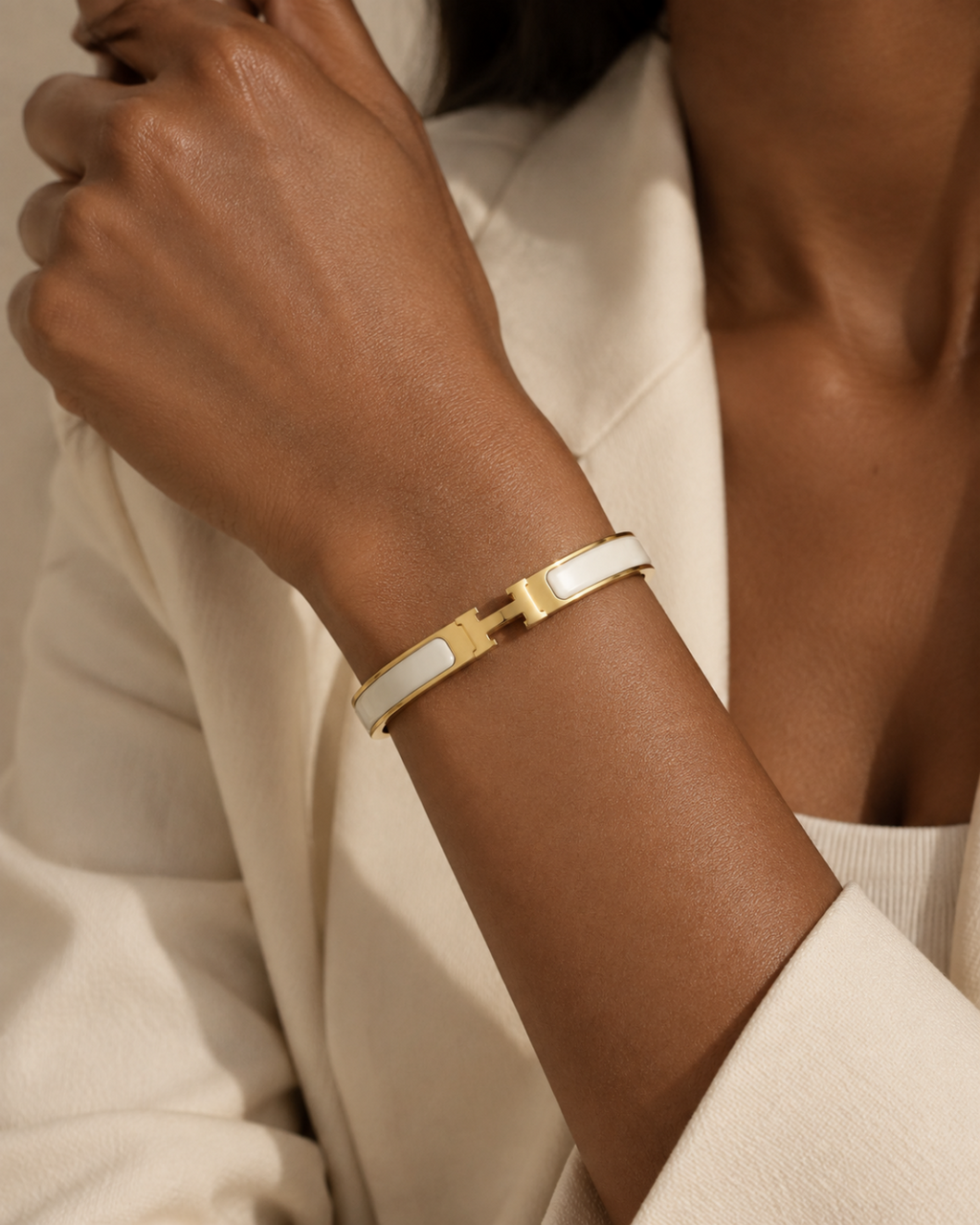 White enamel bangle with gold-tone edges and an H-shaped clasp, close-up of the H-shaped clasp on the wrist.
