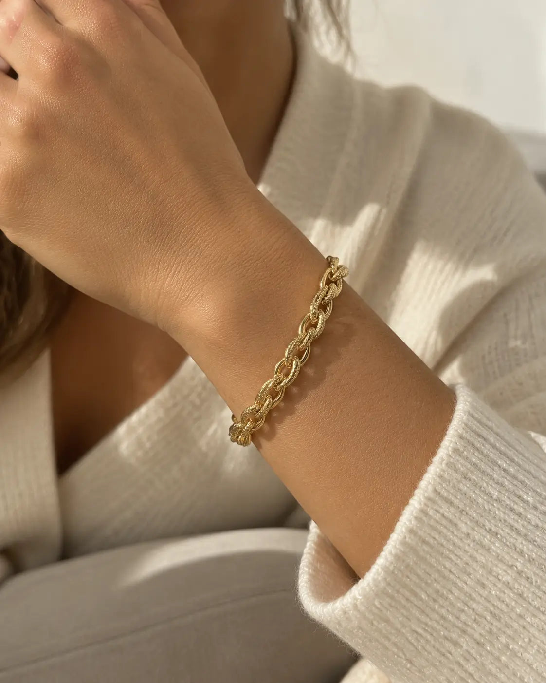Gold-tone bracelet with chunky double links, worn beside a white knitted cuff.