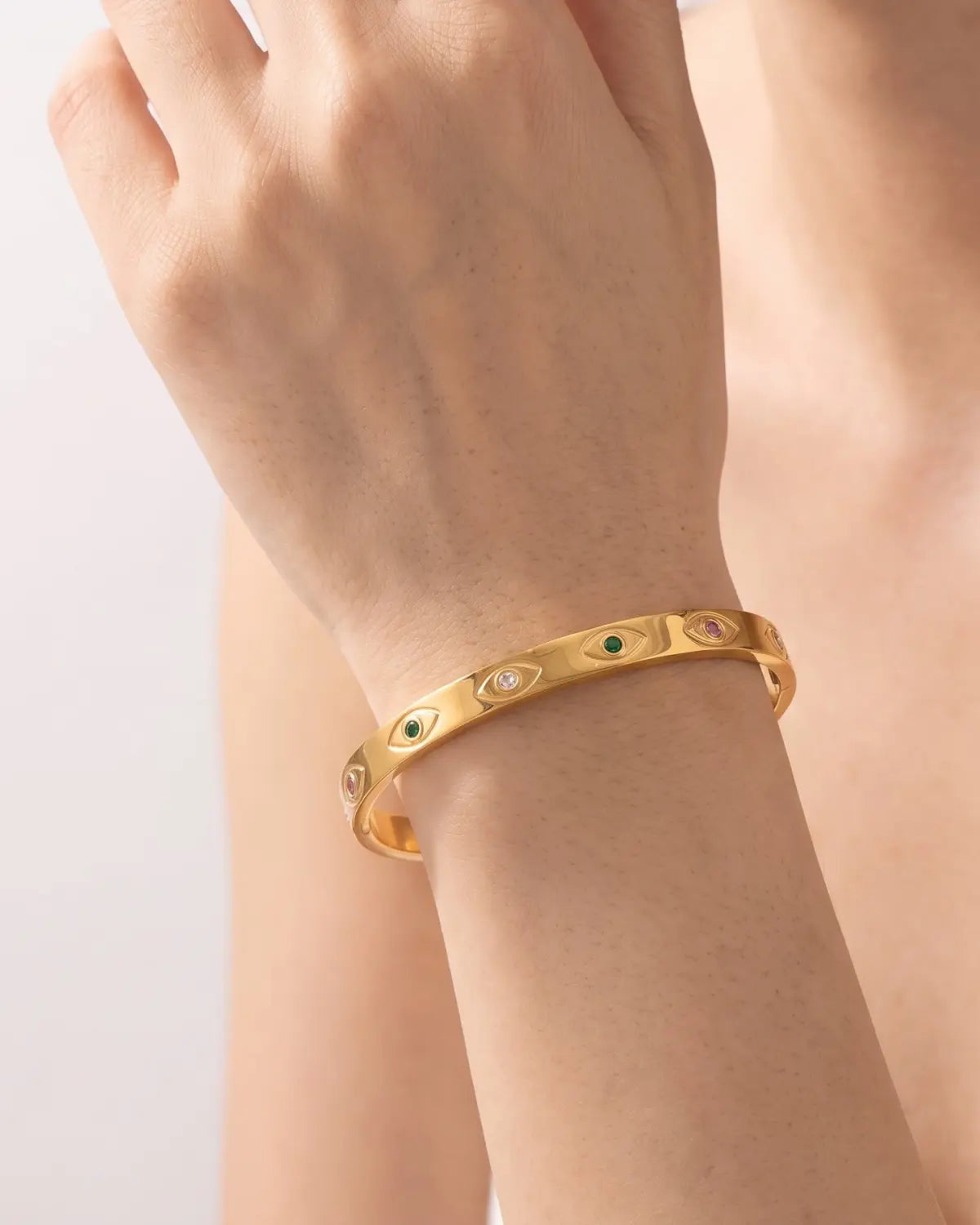 Gold-tone bangle with eye motifs and coloured centres, worn on a raised wrist.