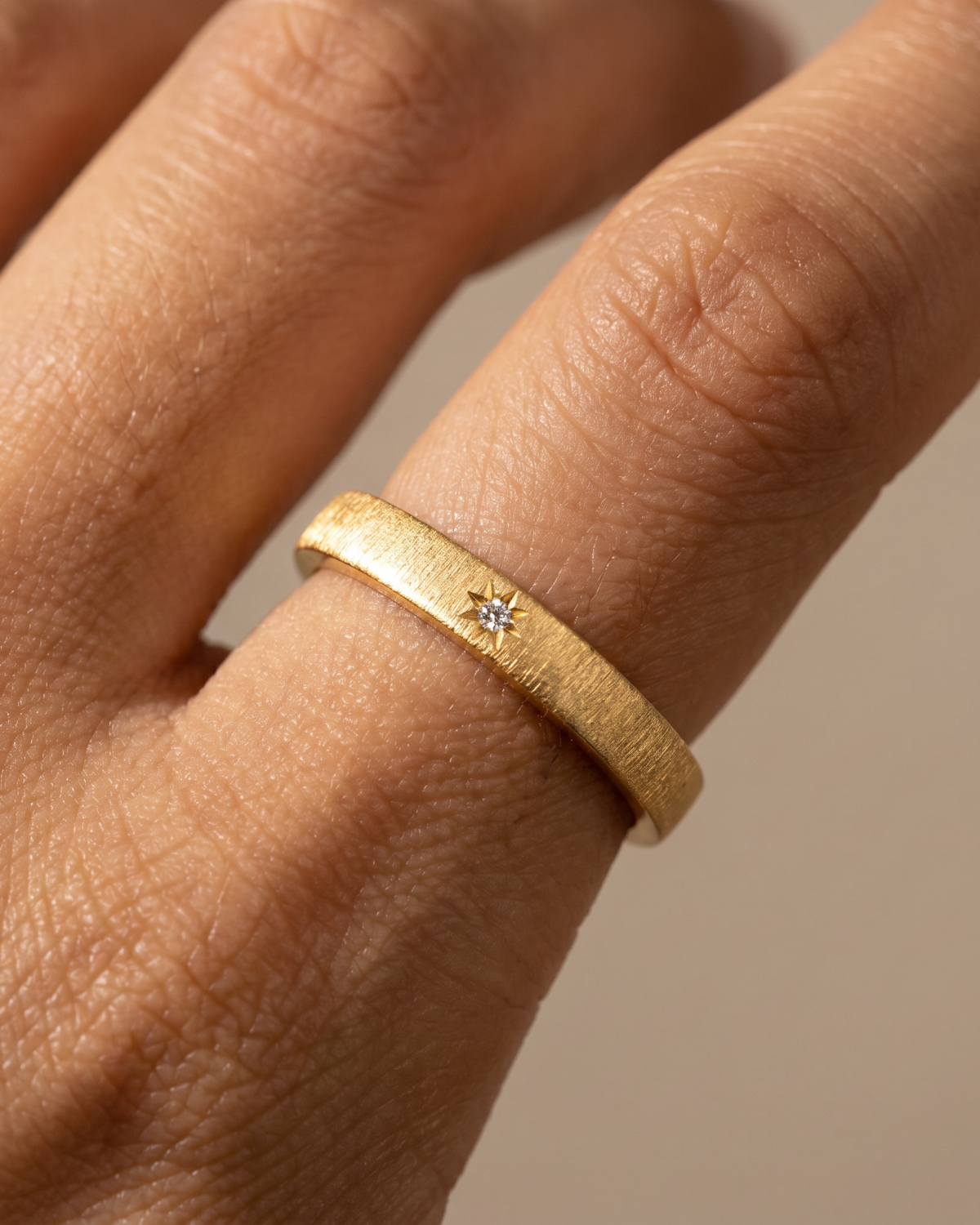 Gold-tone textured ring with a small stone accent, close-up on a finger.