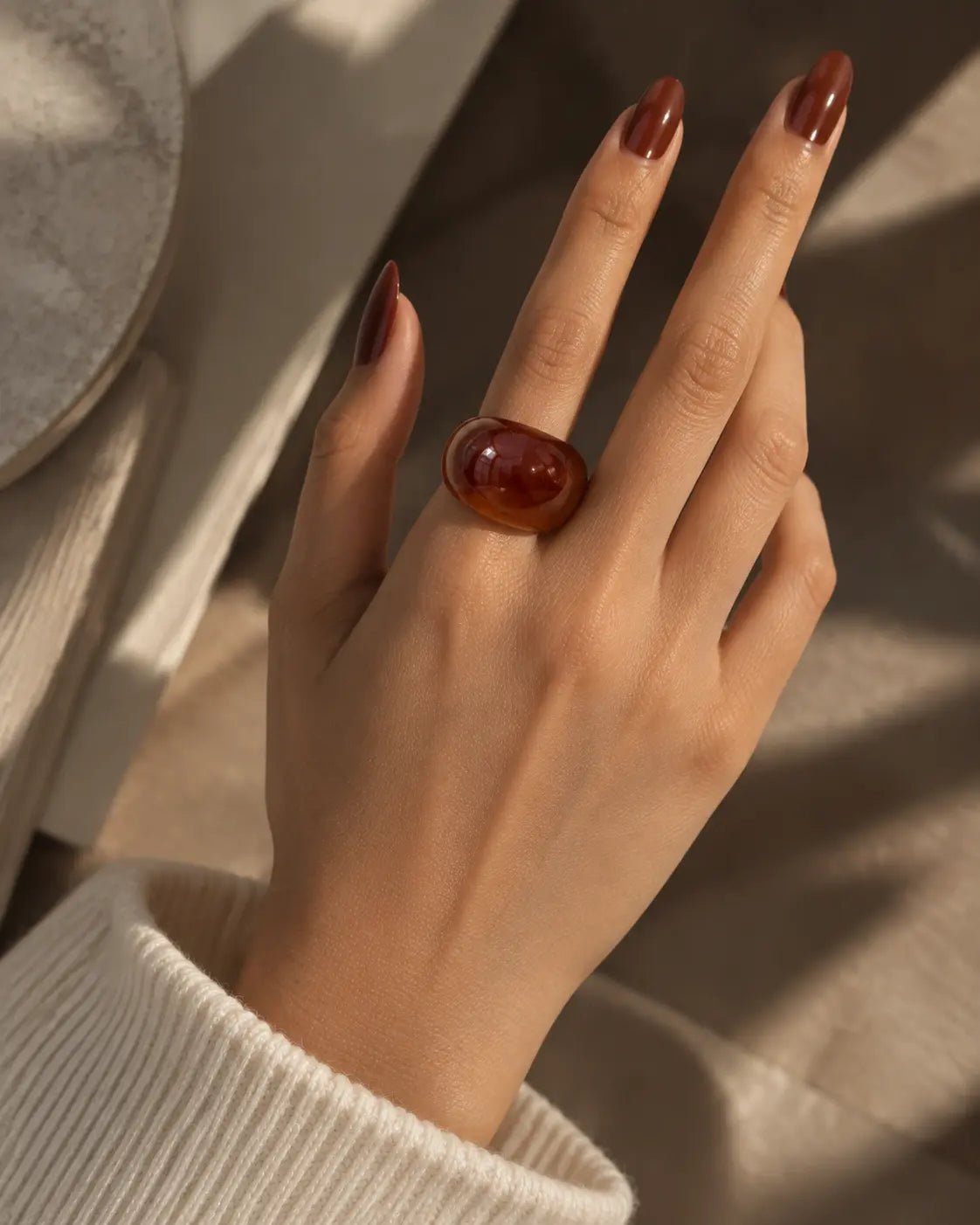 Brown marbled dome ring, worn on a hand resting against light fabric.