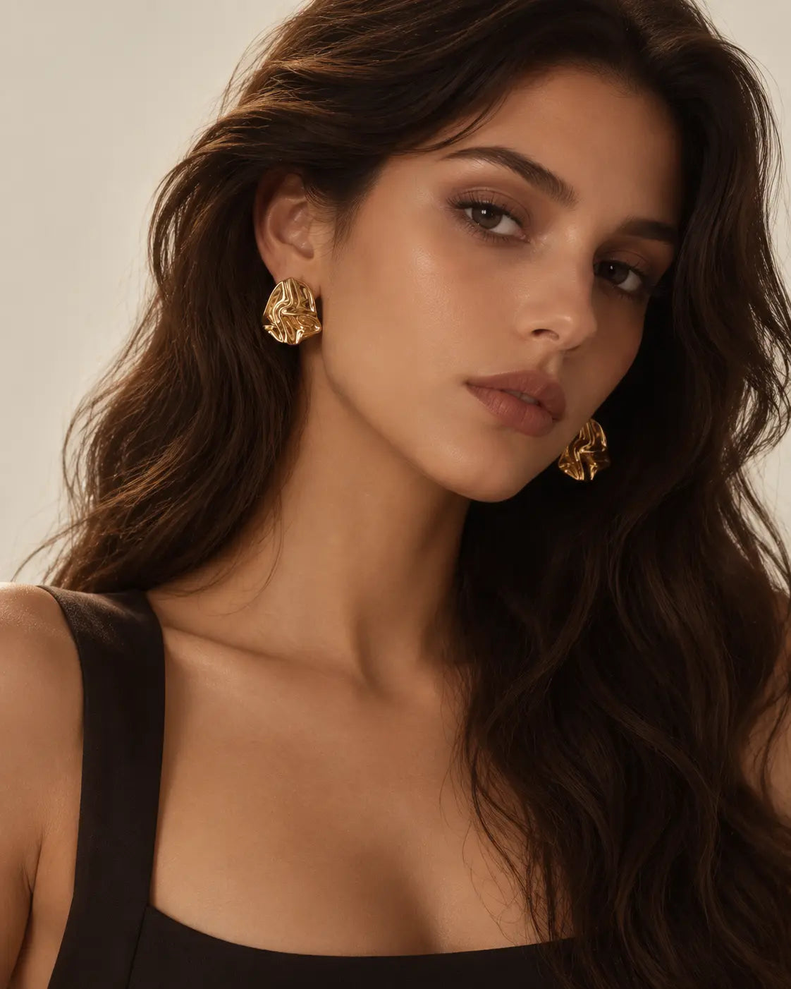 Crumpled gold-tone stud earrings worn in a front-facing portrait.