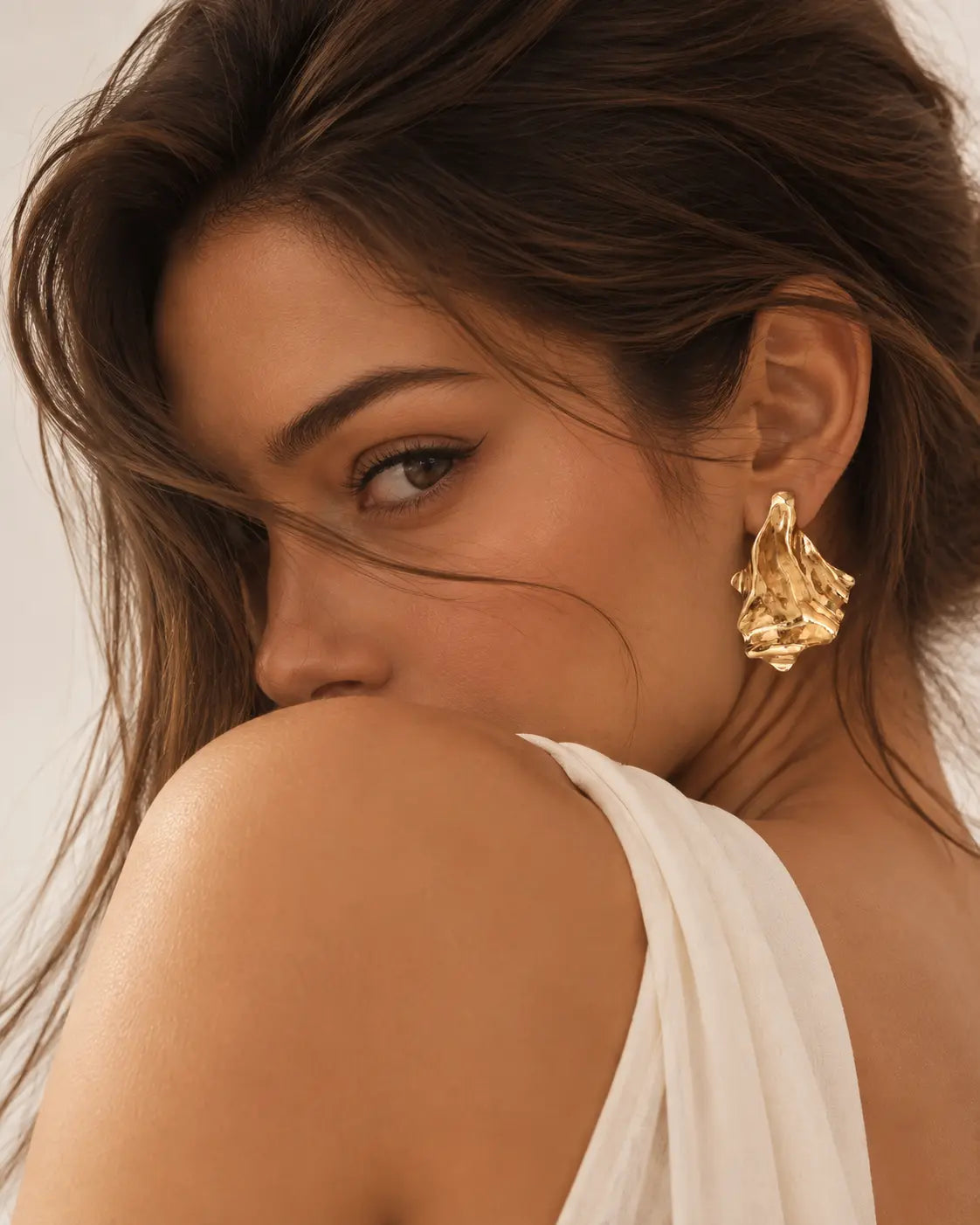 Flared gold-tone earring visible in an over-the-shoulder portrait.