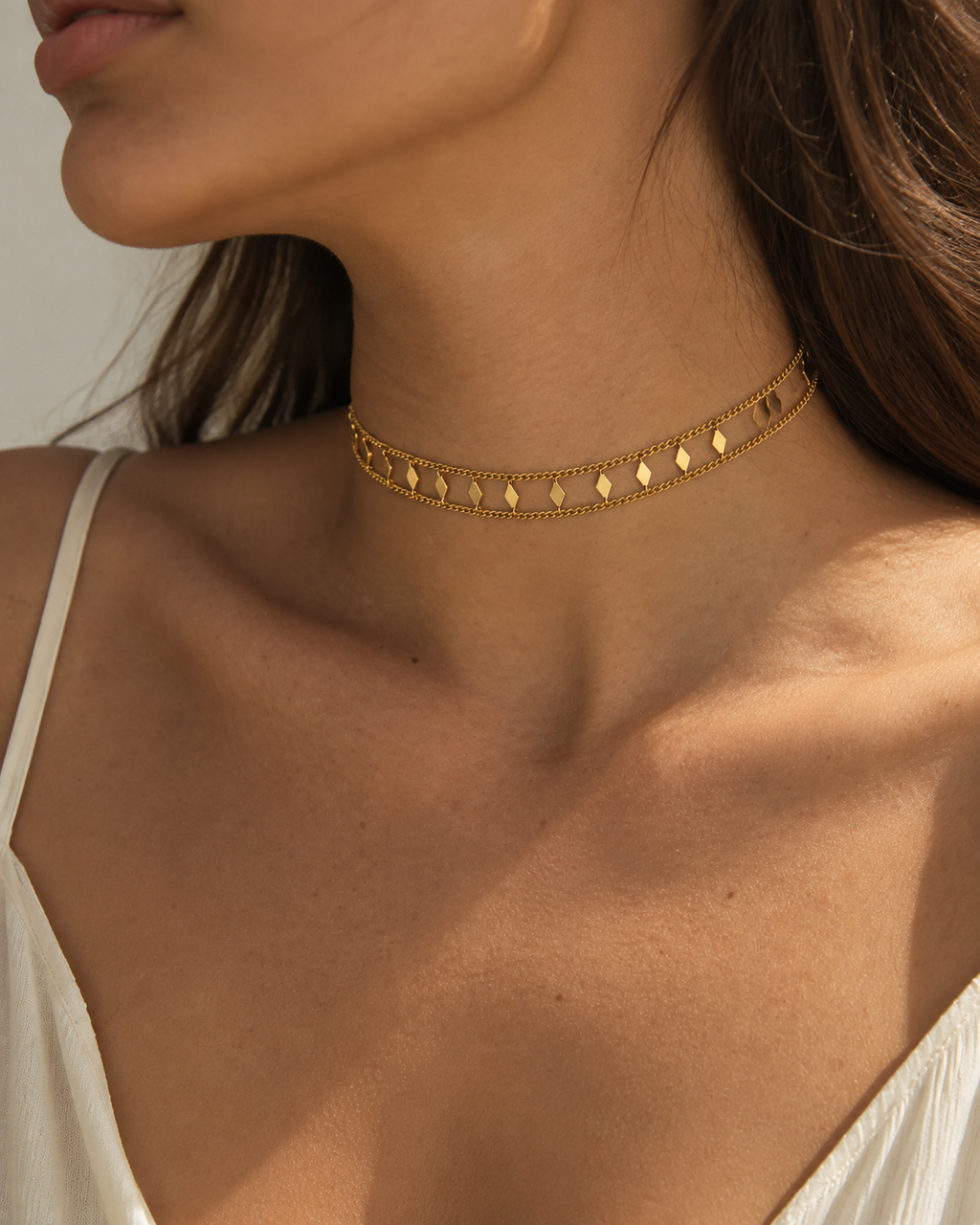 Gold-tone chain necklace with flat accents worn close to the neck in a side view.
