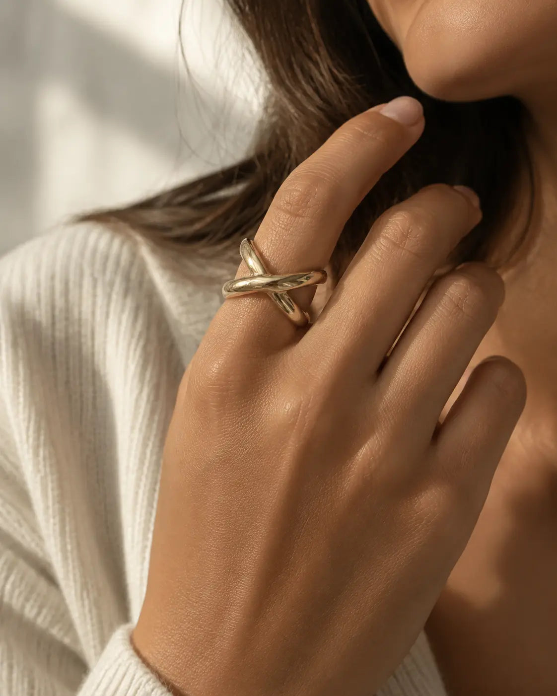 Gold-tone open ring with chunky crossover bands, worn on a hand near the chin.