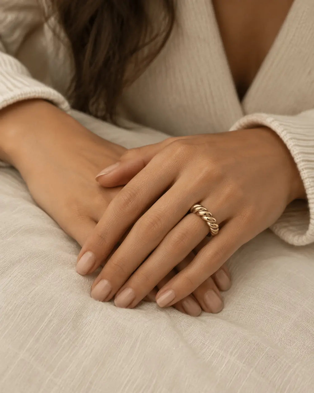 Gold-tone open band ring with a cable-twist pattern, worn with hands resting together.