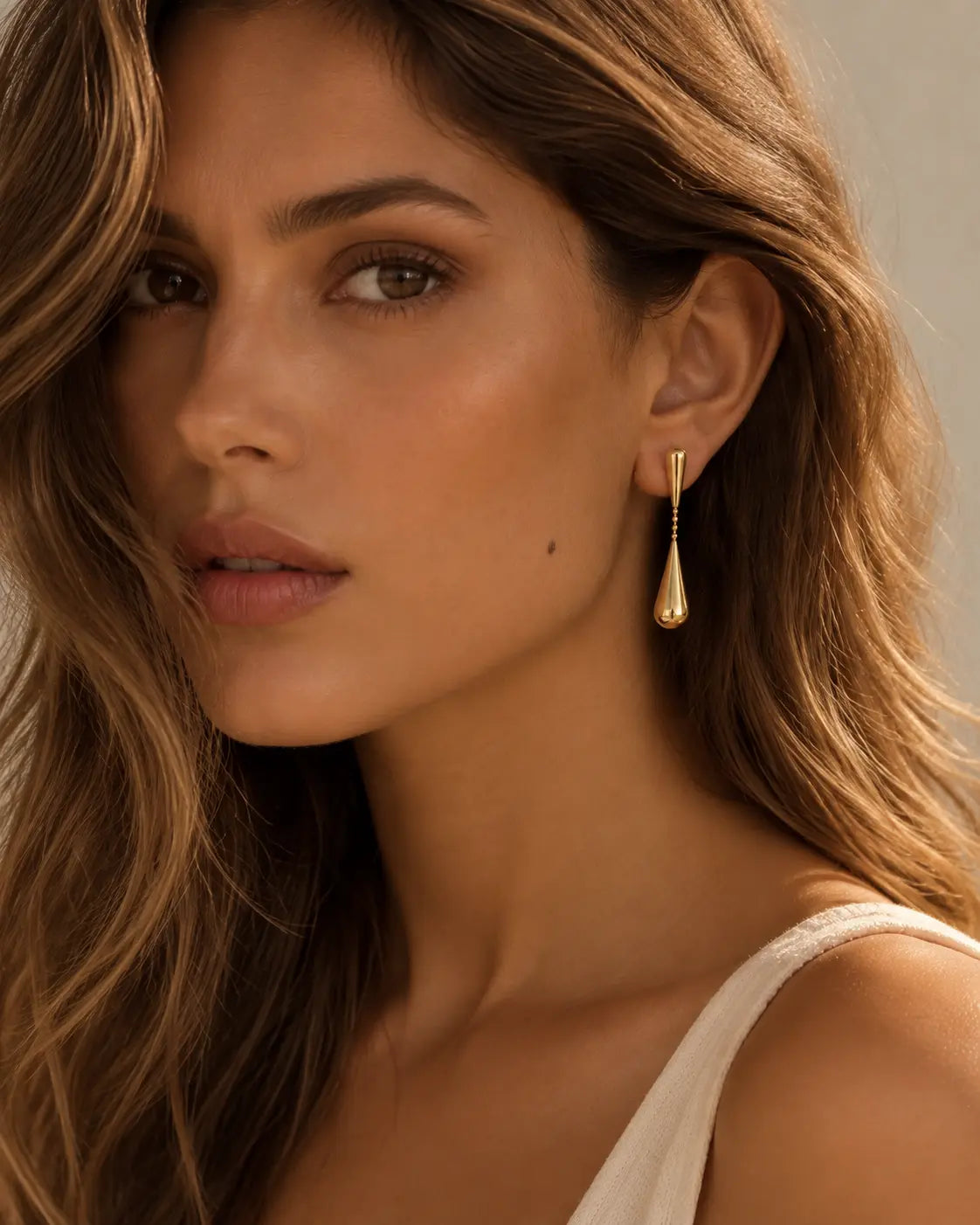 Linked gold-tone teardrop earrings worn in a three-quarter portrait.