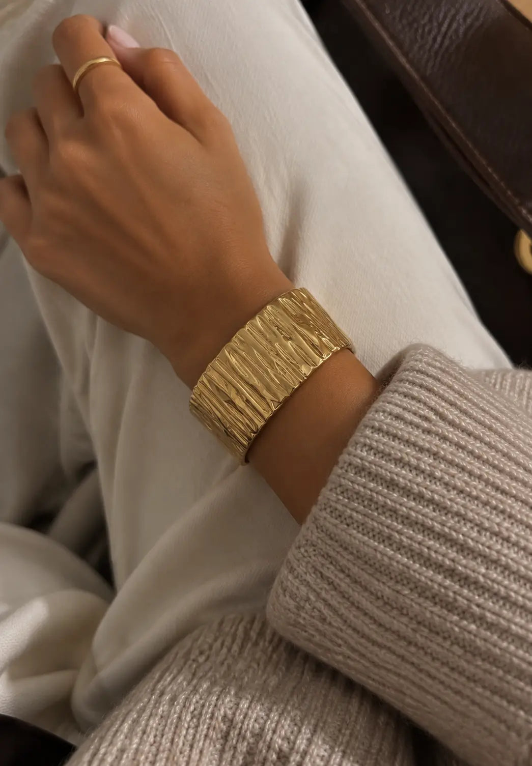 Wide gold-tone cuff bangle with a bark-like texture, worn on an arm resting across the lap.