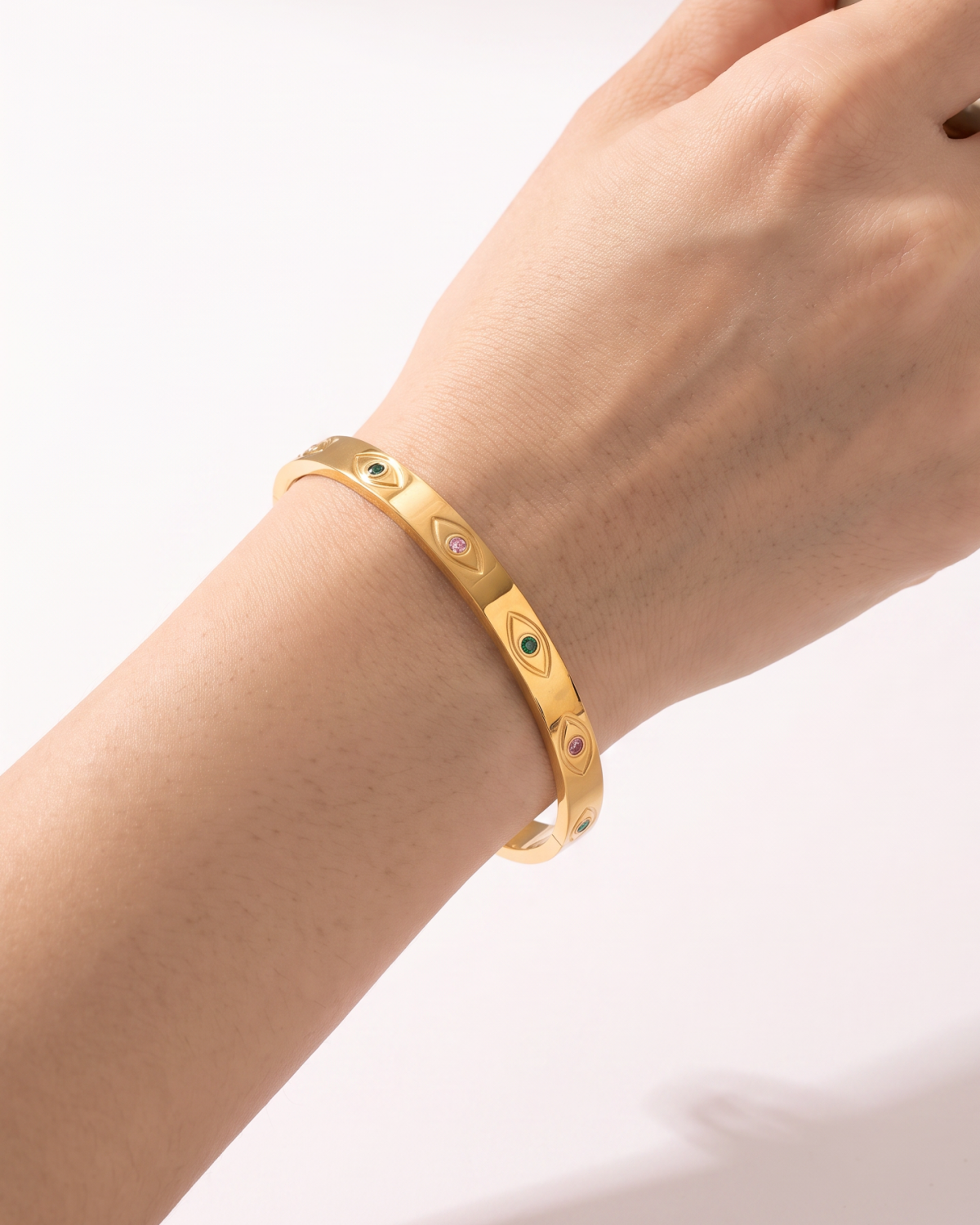 Gold-tone bangle with eye motifs and coloured centres, side view on the wrist.