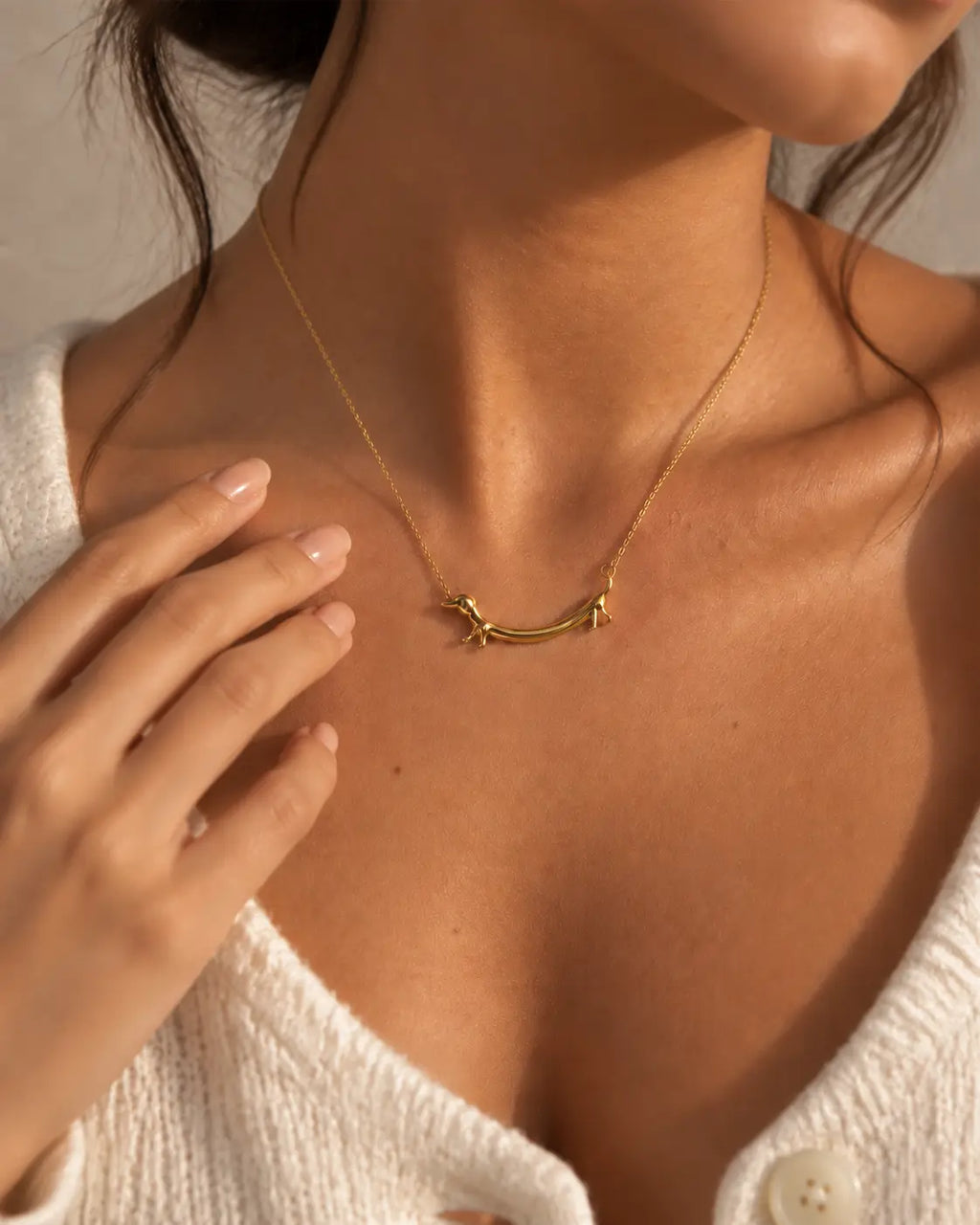 Gold-tone necklace with a dachshund-shaped pendant, worn with a hand beside the dog-shaped pendant.