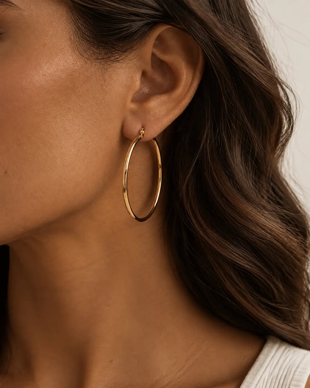 Close-up of a slim gold-tone hoop earring on the ear.