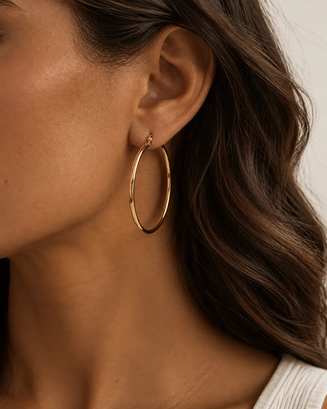 Close-up of a slim gold-tone hoop earring on the ear.