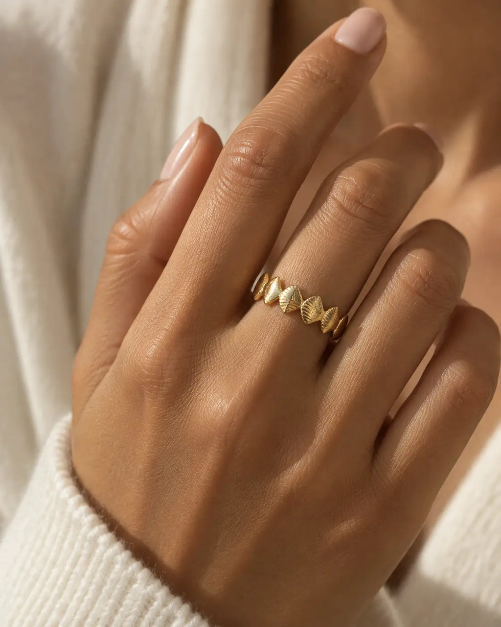 Gold-tone band ring with textured rhombus-shaped motifs, worn on a raised hand.