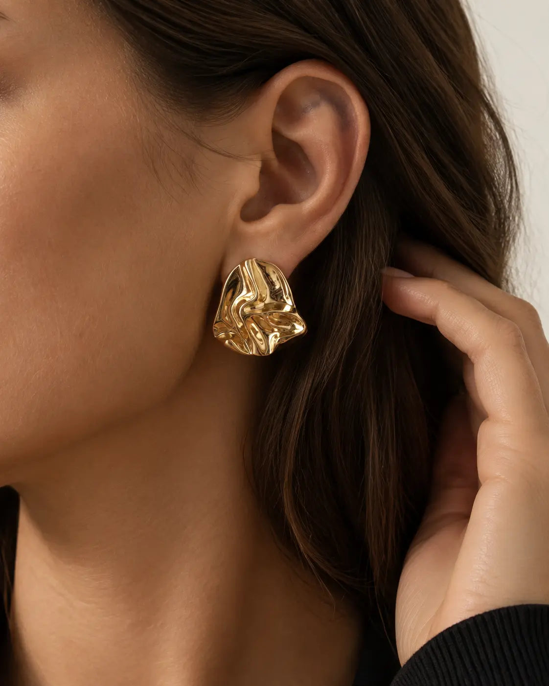 Close-up of a crumpled gold-tone stud with a hand beside the hair.