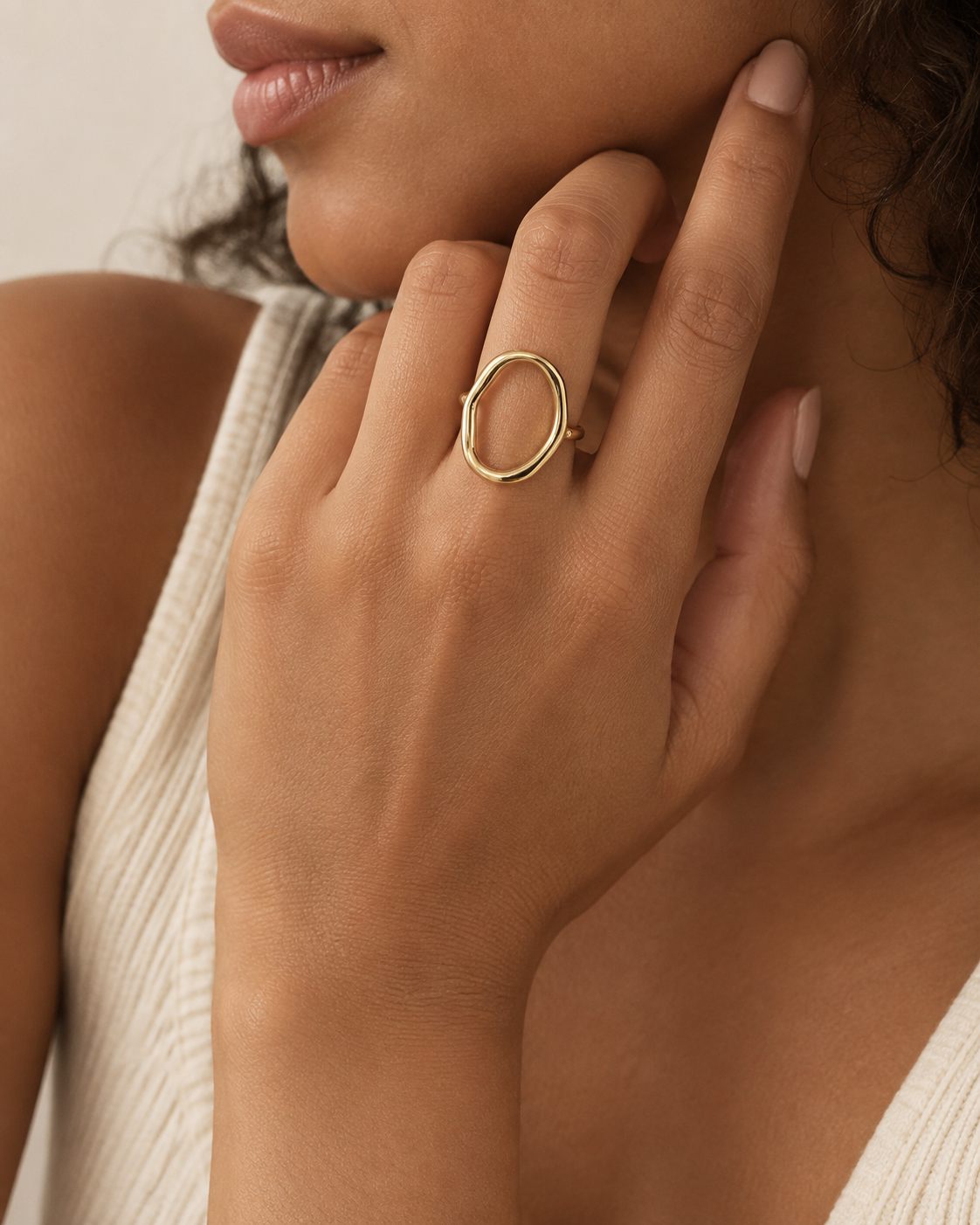 Gold-tone open ring with a tall hollow oval outline, worn with fingers beside the cheek.
