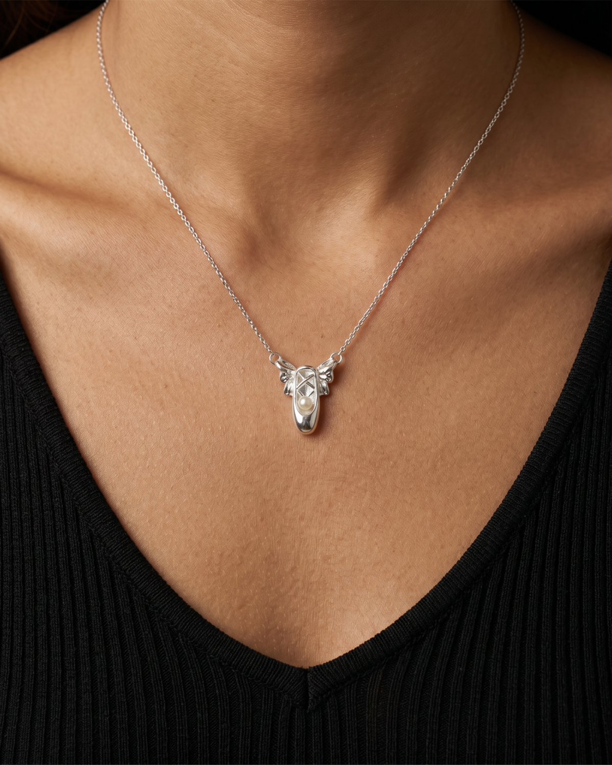 Silver-tone necklace with two ballet-slipper pendants, close-up worn with a black V-neck top.