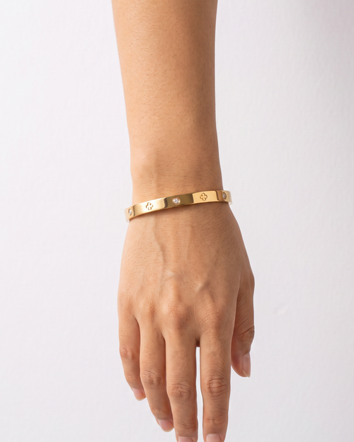 Gold-tone bangle with clover outlines and stone accents, worn on a straight forearm.