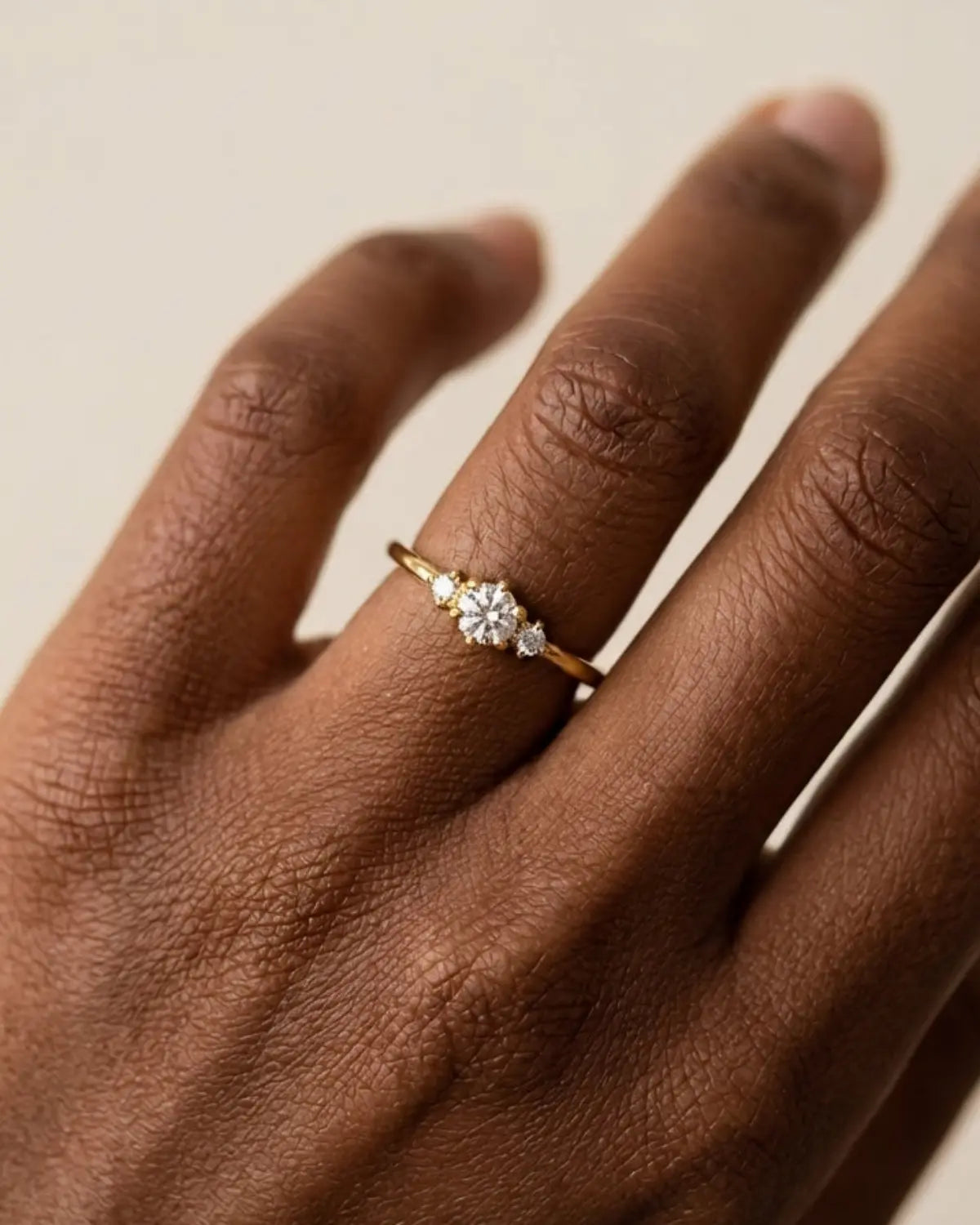Gold-tone band ring with a central three-stone cluster, worn with the back of the hand facing the camera.