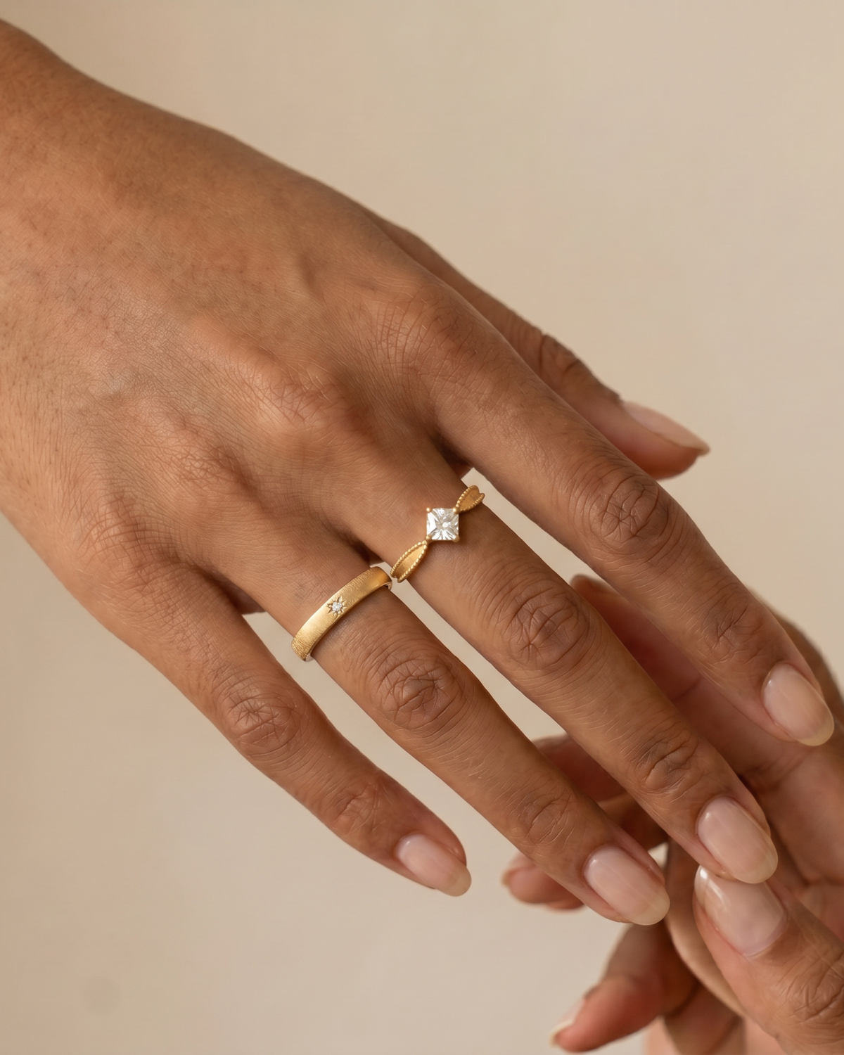 Gold-tone textured ring with a small stone accent, worn beside a separate stone-accent ring in a styling image.