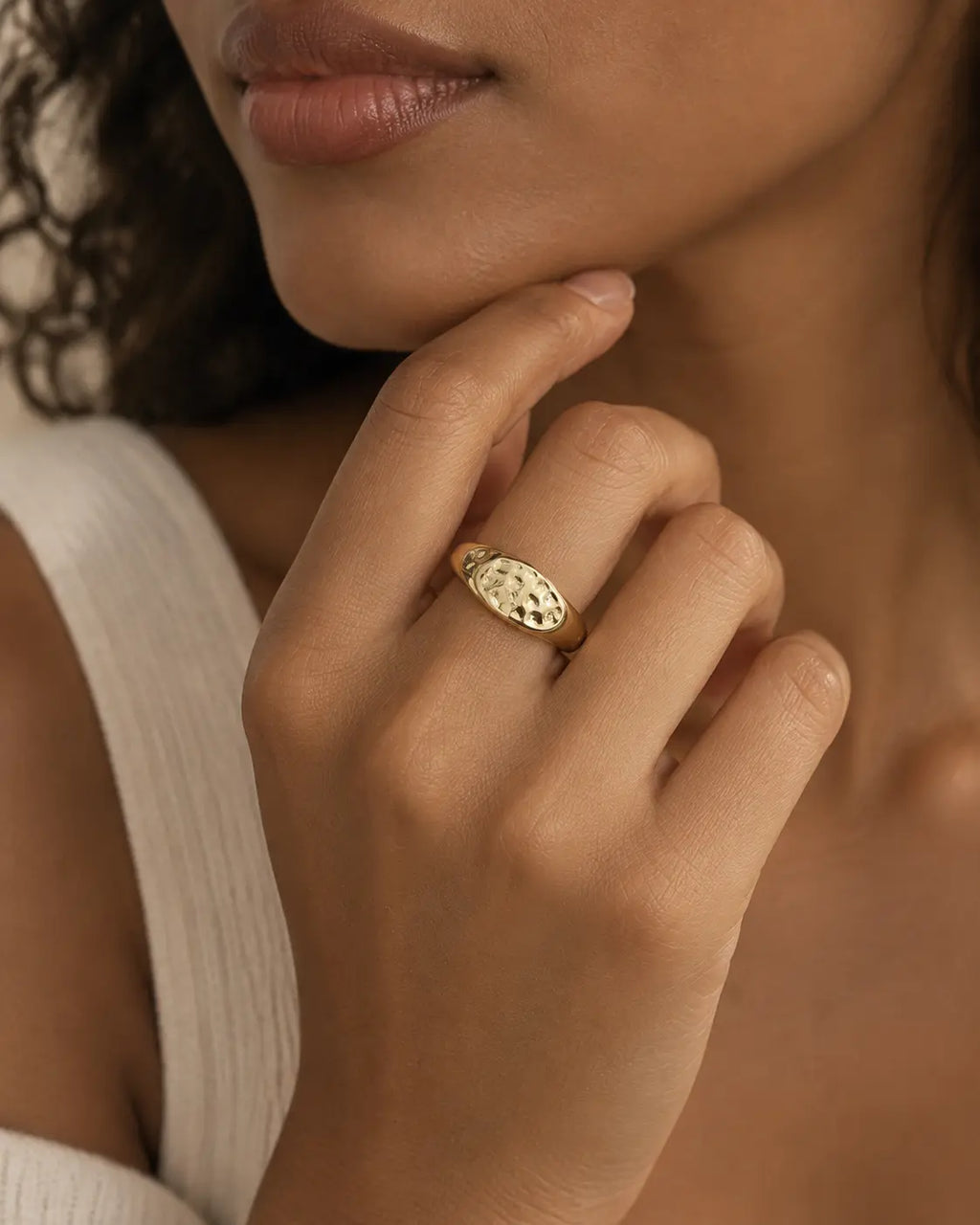 Gold-tone ring with a hammered oval dome, worn on a hand near the chin.