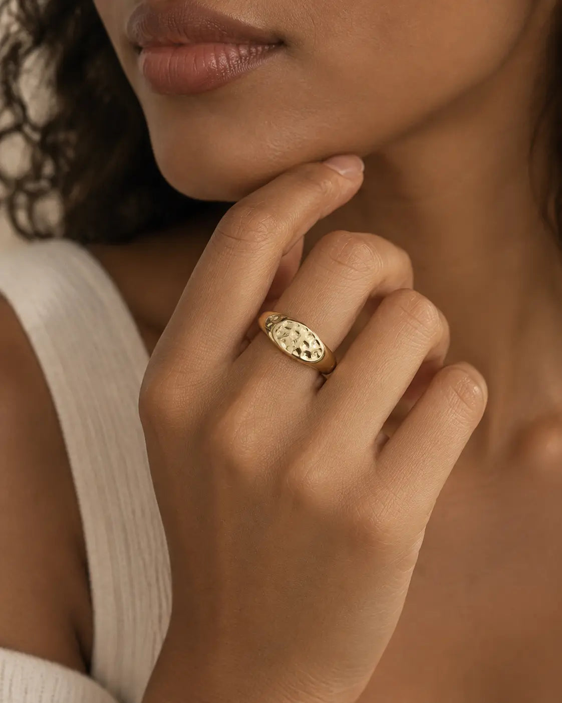 Gold-tone ring with a hammered oval dome, worn on a hand near the chin.